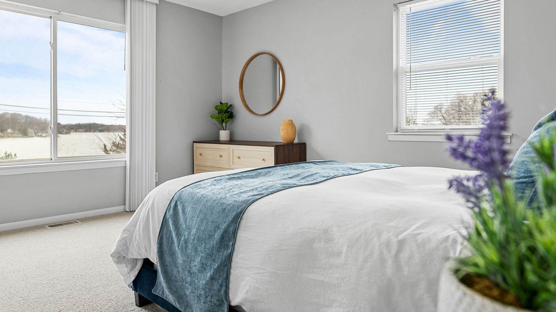 Bright bedroom with a bed, dresser, mirror, and large windows letting in daylight.