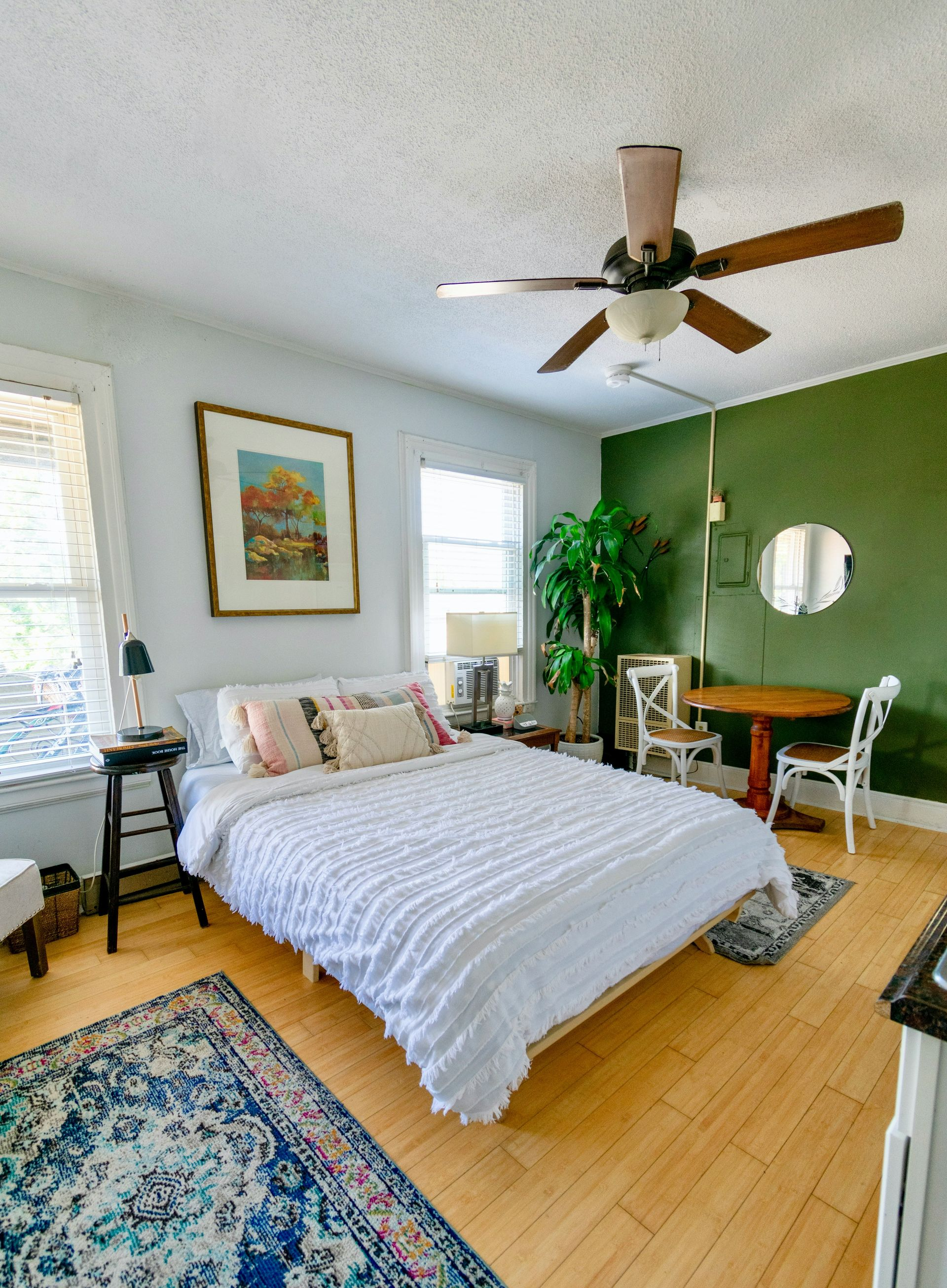 Bright bedroom with a bed, green accent wall, ceiling fan, and colorful rug on wood floors