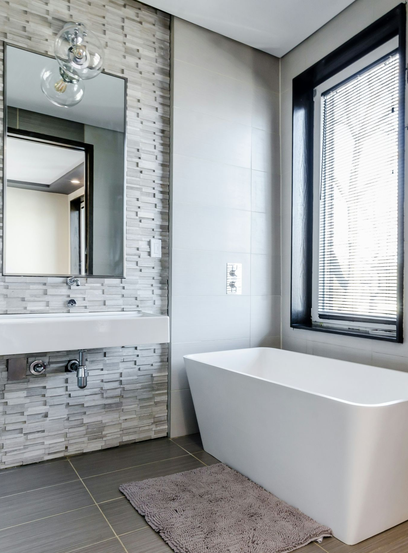 Modern bathroom with freestanding tub, large mirror, tiled wall, and black-framed window