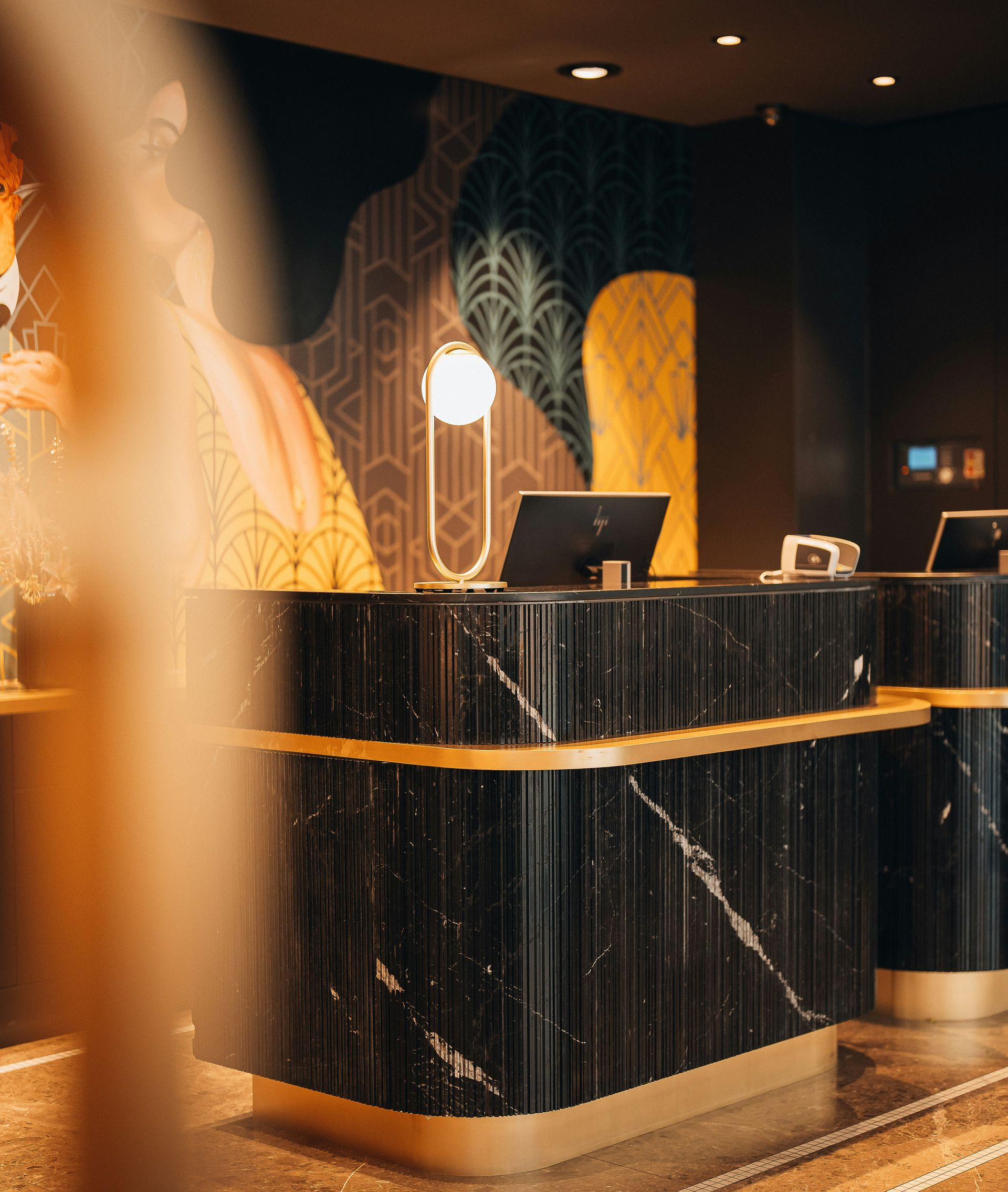 Art deco style hotel reception desk made of black marble with gold accents, set against a patterned feature wall.