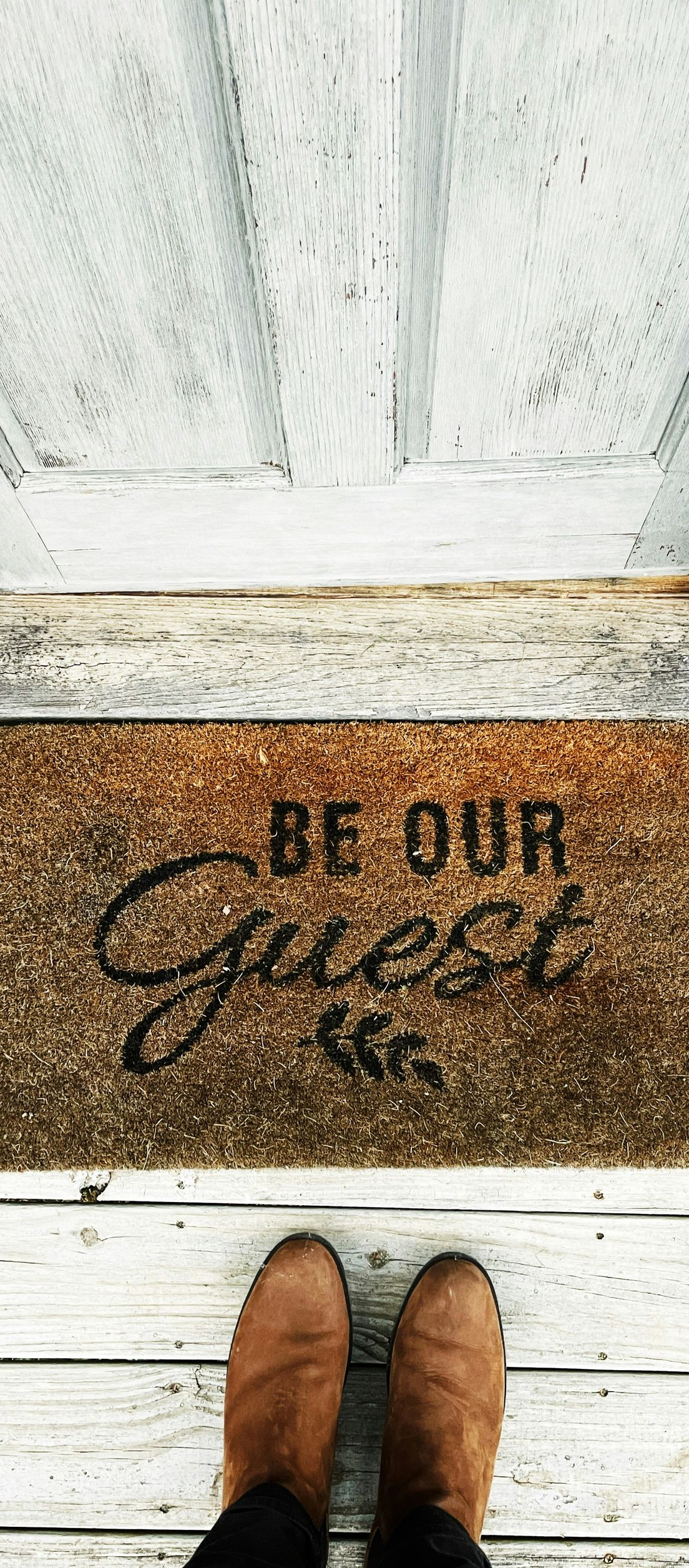 be our guest? doormat on white porch with brown boots at the doorstep