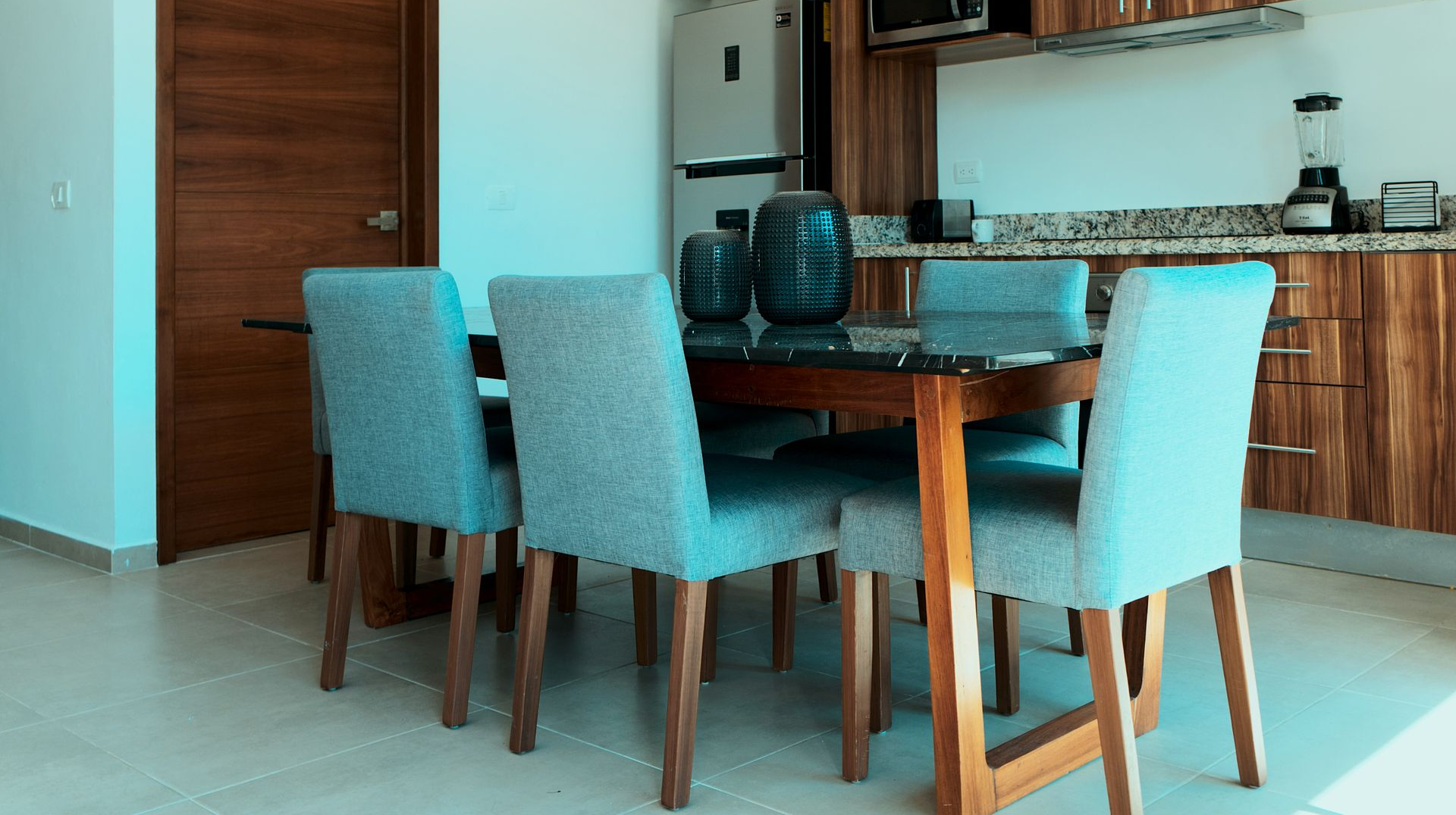 Modern kitchen and dining area with wooden table, teal chairs, and stainless steel appliances.