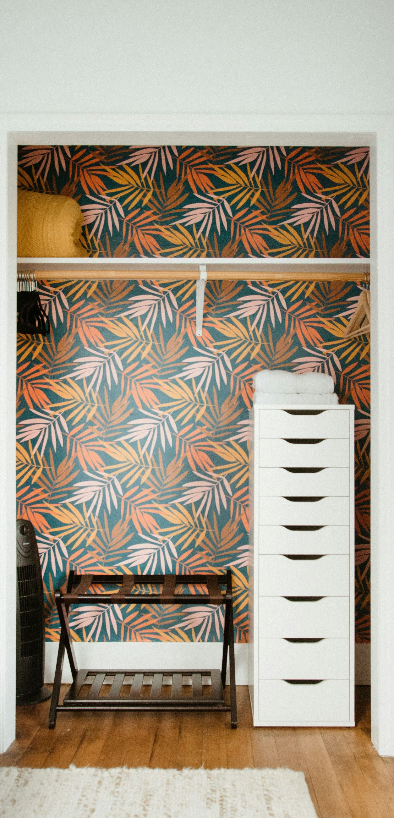 Small room with tropical wallpaper, wooden chair, and white drawer cabinet on hardwood floor.