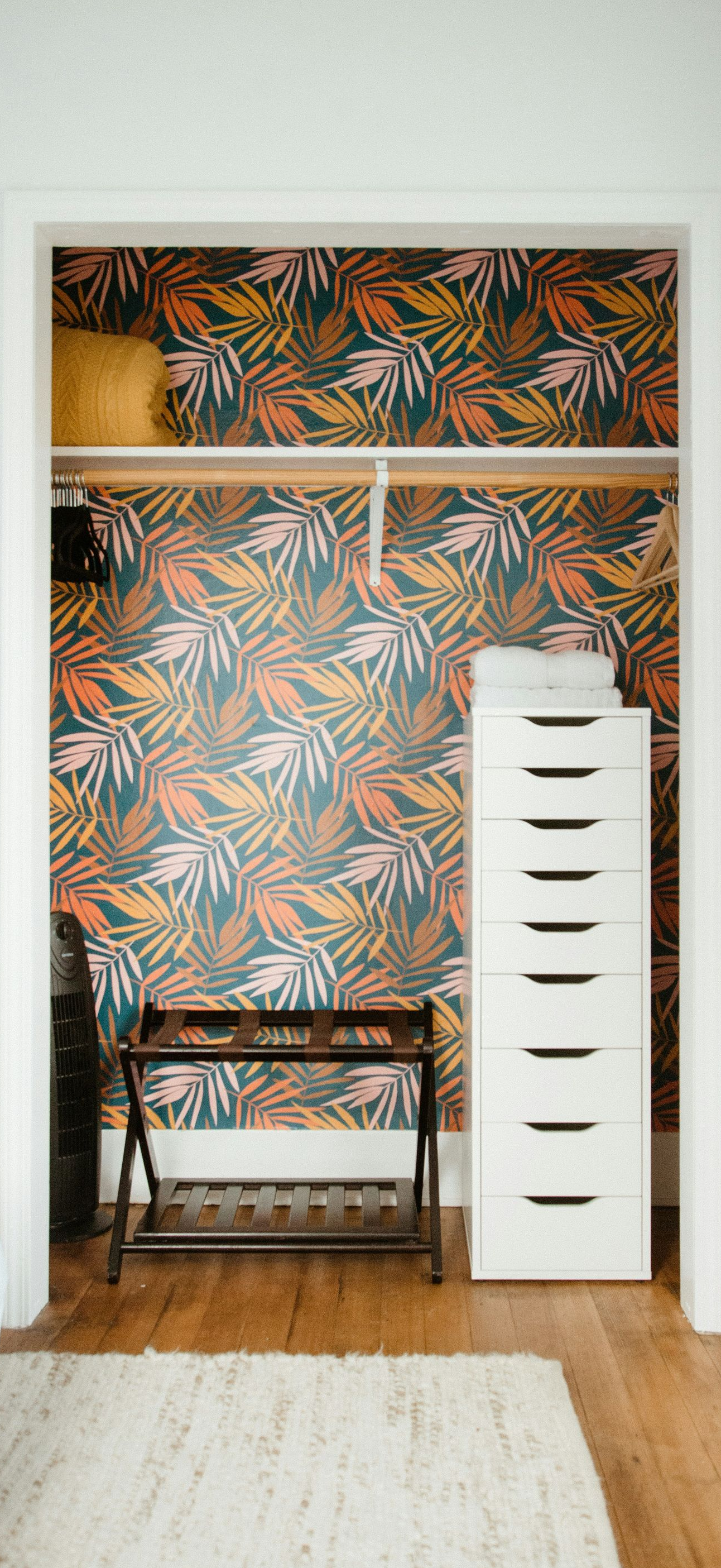 Built-in closet nook with patterned wallpaper, bench, and white drawer tower in a doorway alcove