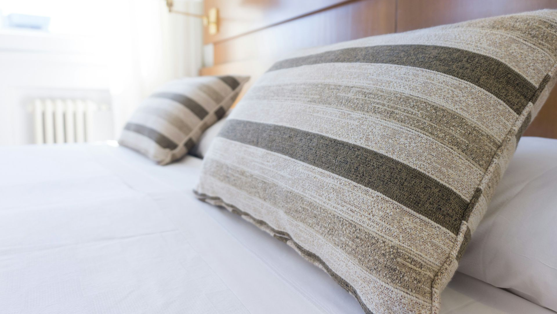 Striped pillows on a neatly made white bed in a bright bedroom