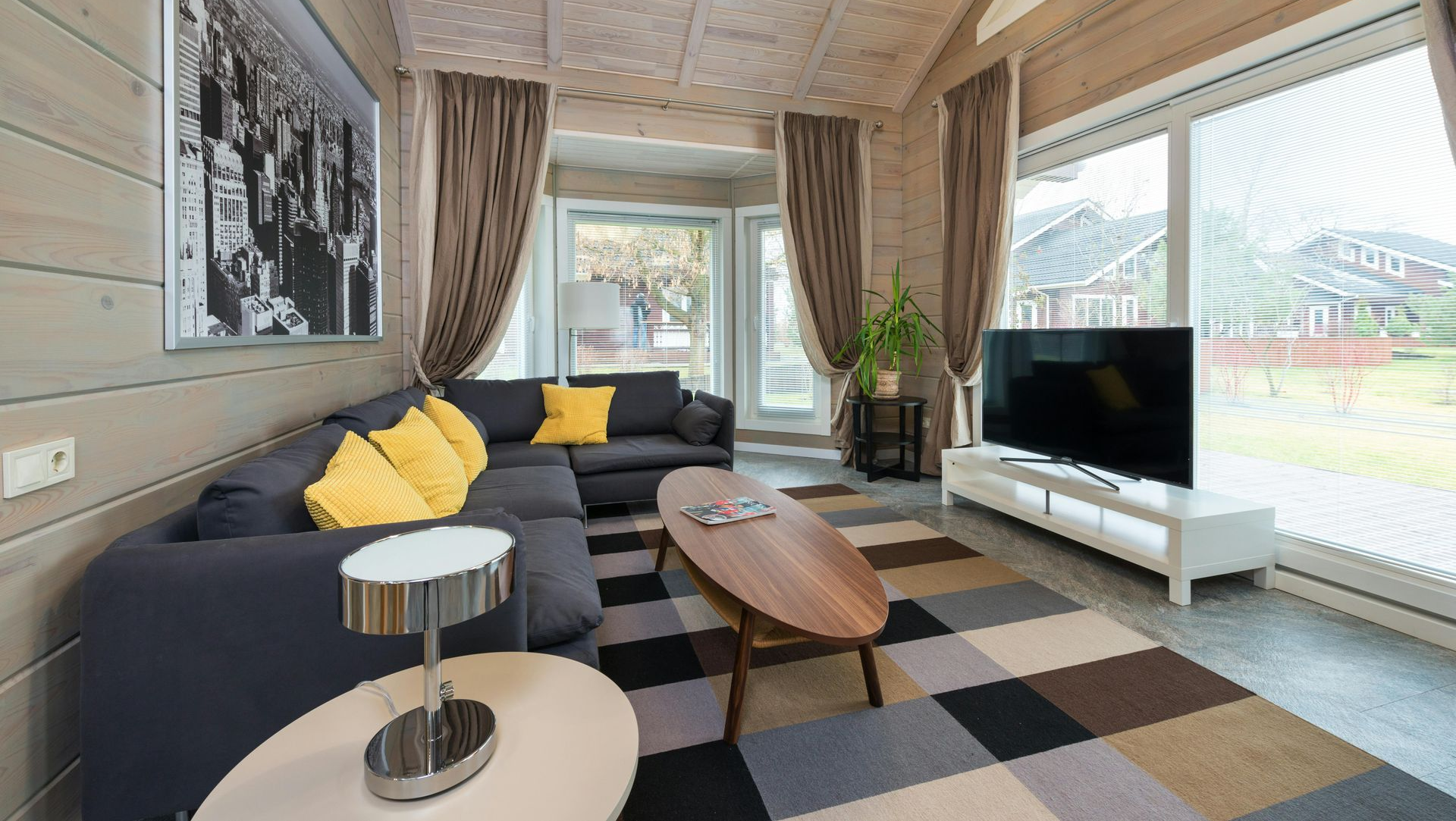 Living room with a gray sectional, yellow pillows, and large windows.  A black and white photo hangs on the wall.
