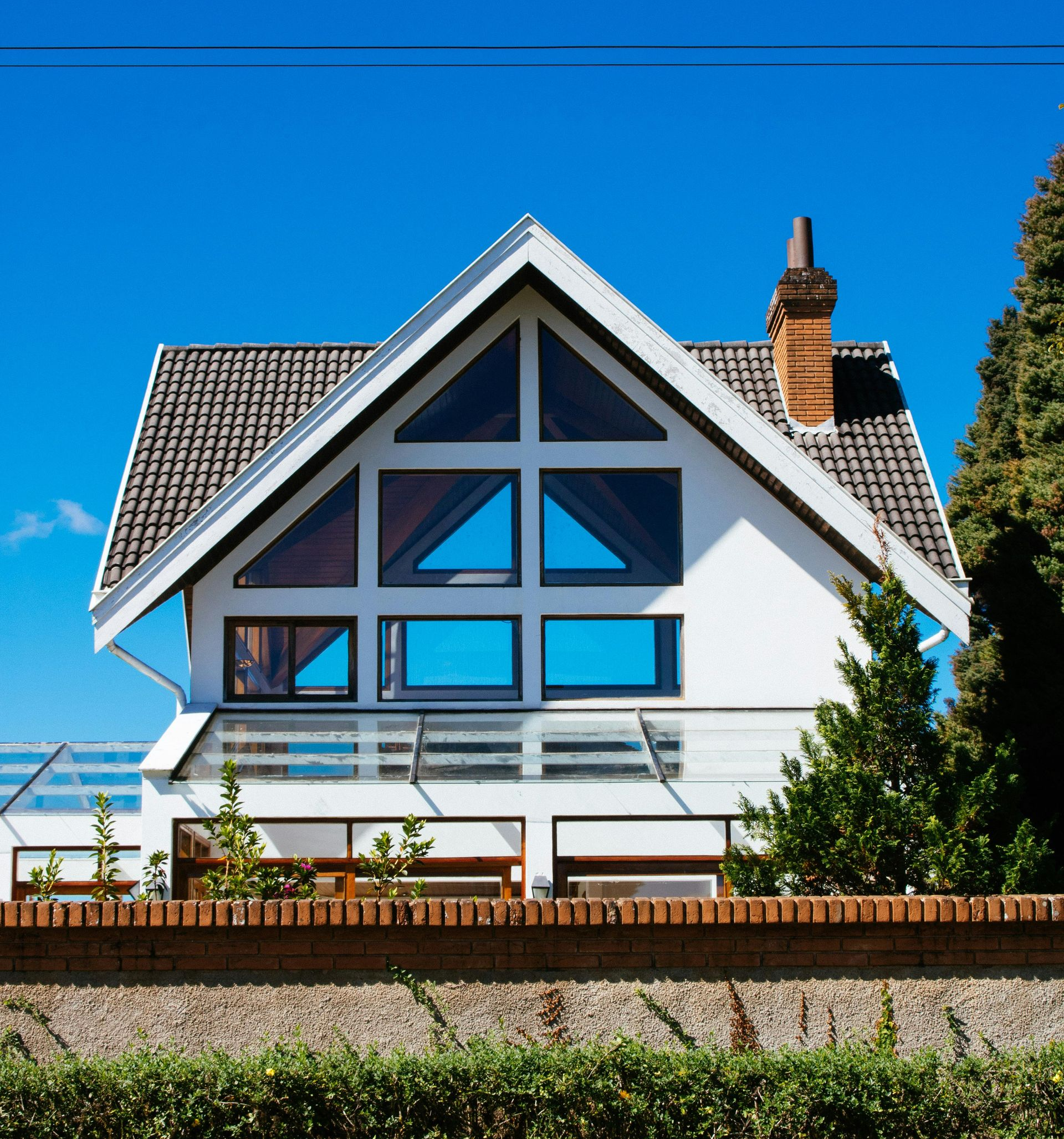 White house with large triangular windows, a brick chimney, and a tiled roof, against a clear blue sky.