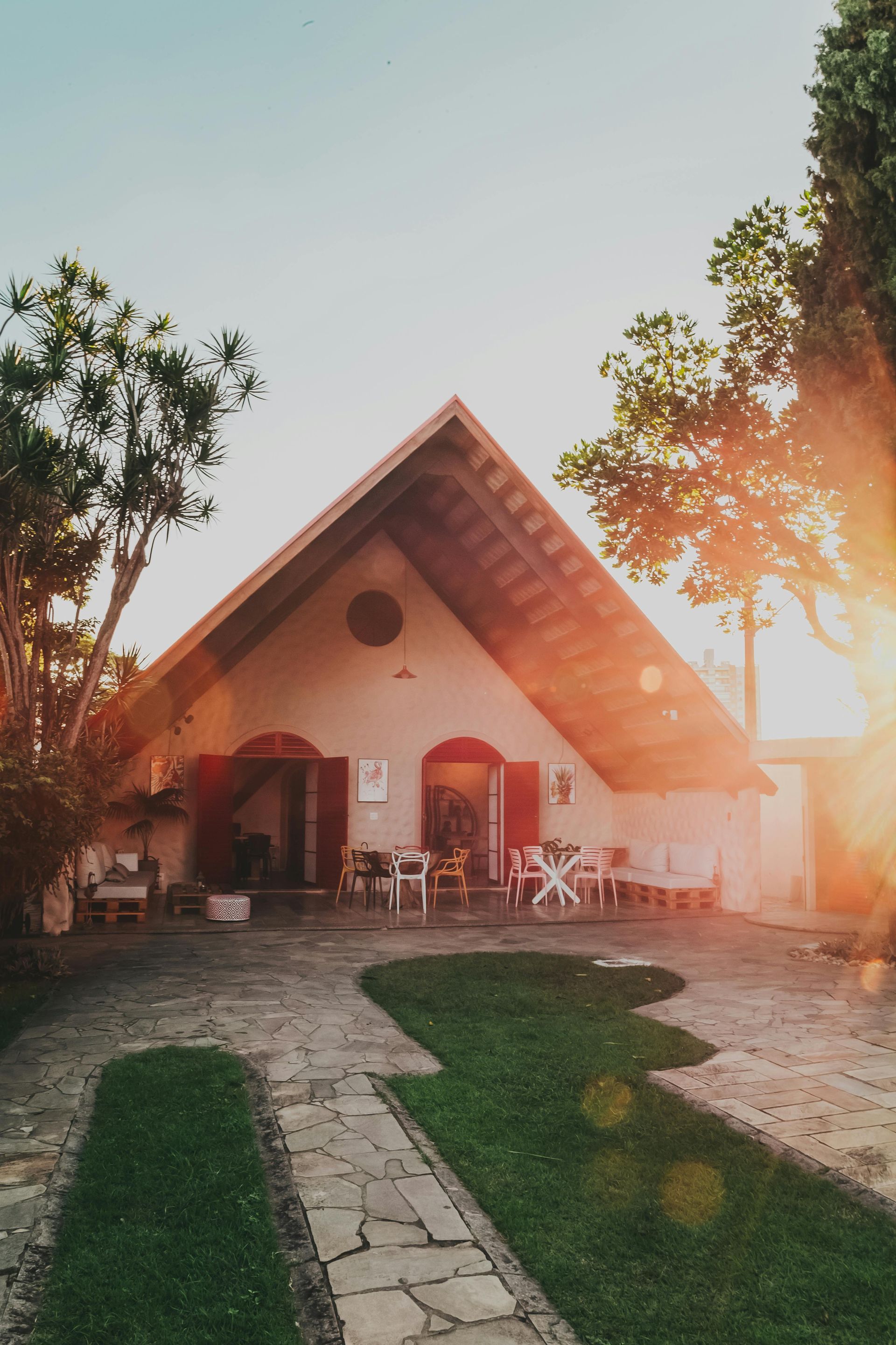 Quaint beige building with a gabled roof, stone path, and outdoor seating, illuminated by the setting sun.