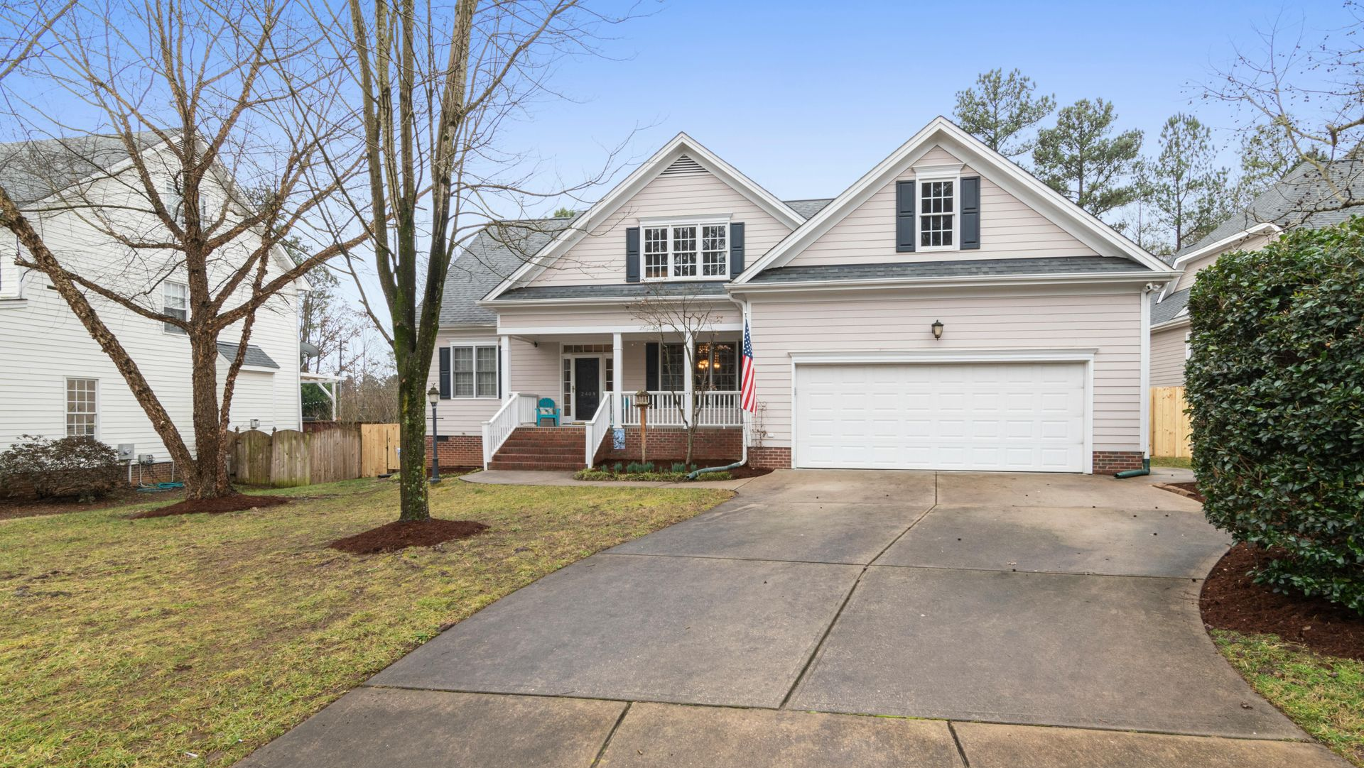 Gray house with a two-car garage, porch, and a concrete driveway. Trees are bare, it's a cloudy day.