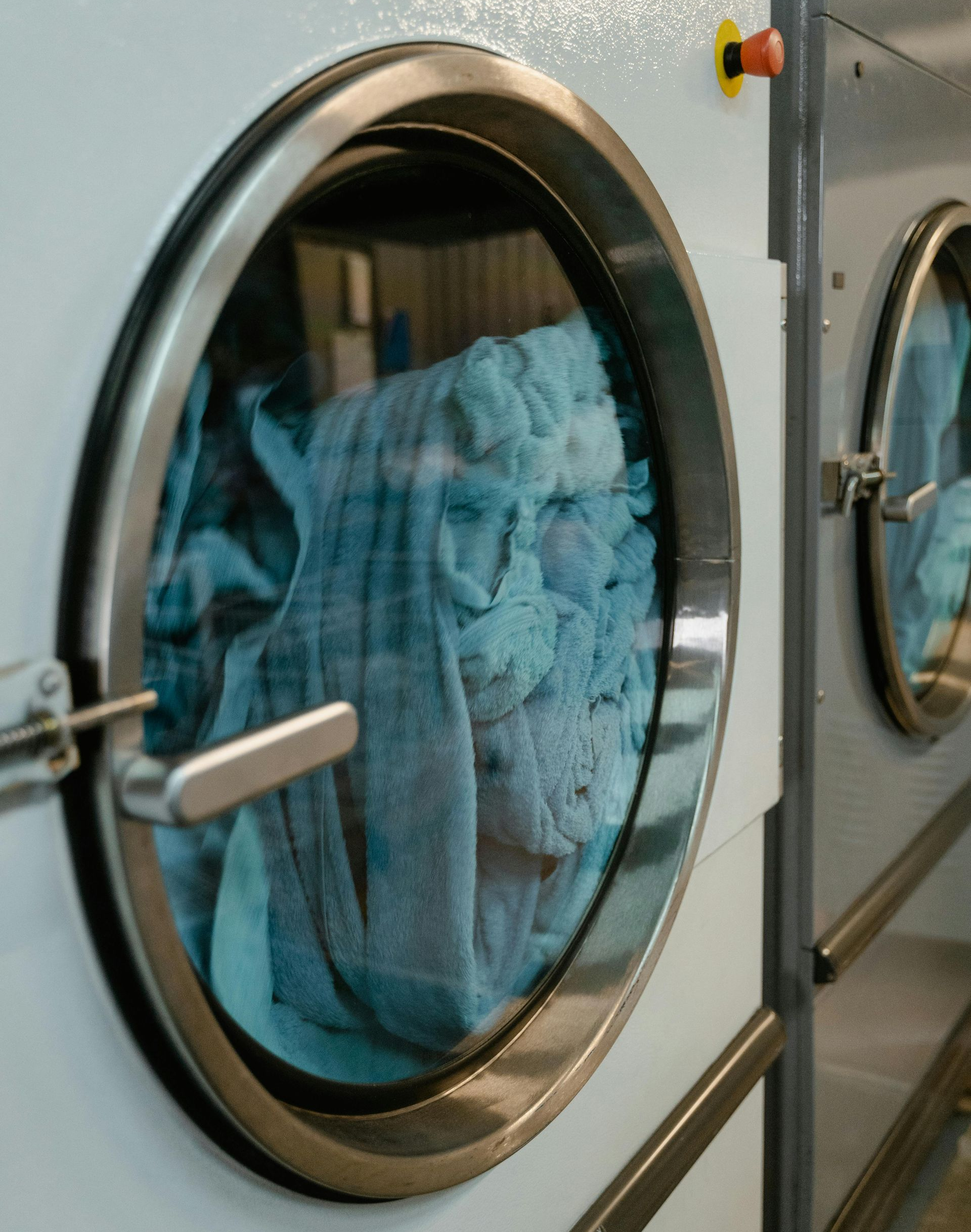 Close-up of a commercial dryer with a clear door; blue fabric tumbling inside.