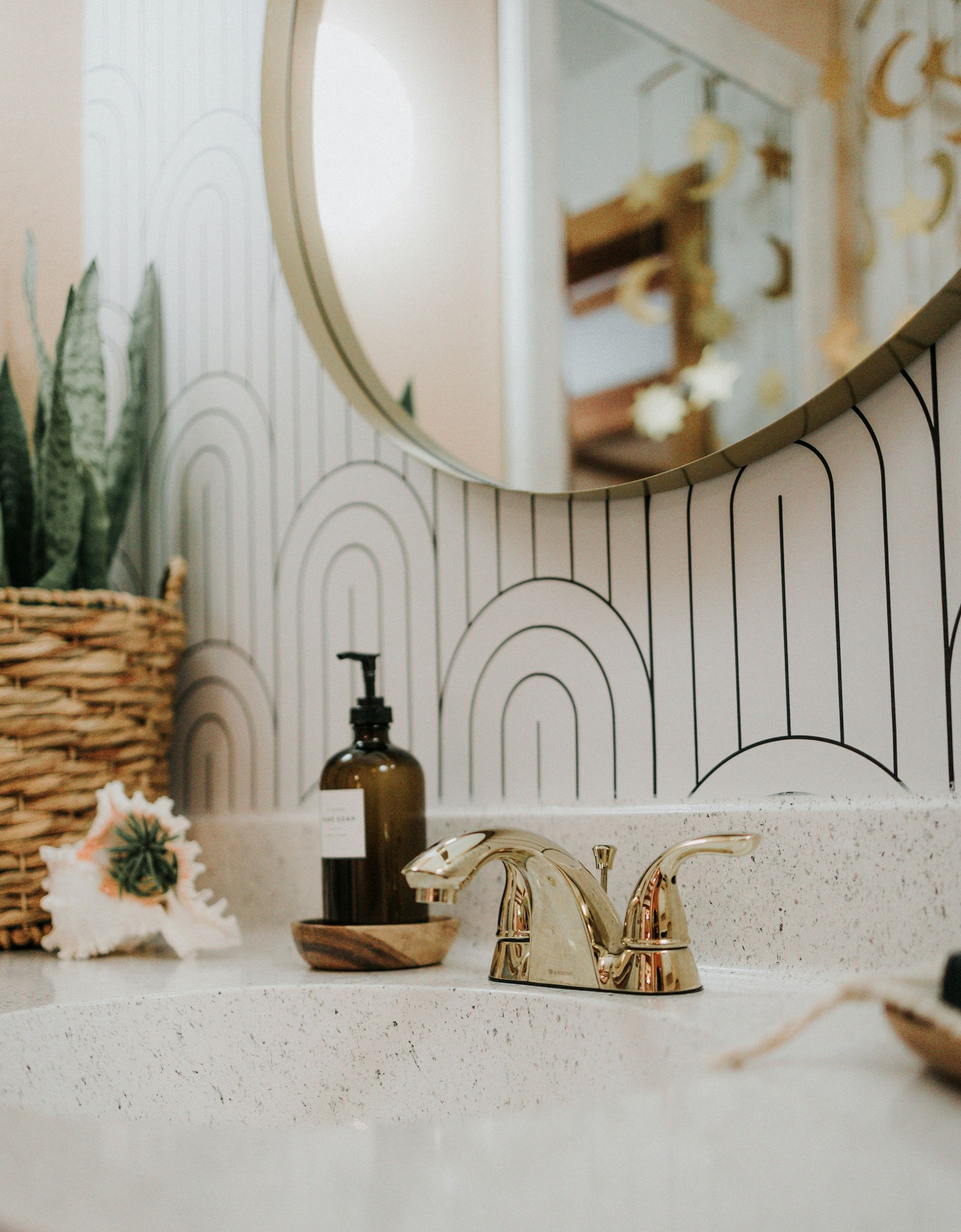 Bathroom vanity with gold faucet, round mirror, and amber bottle beside a potted plant