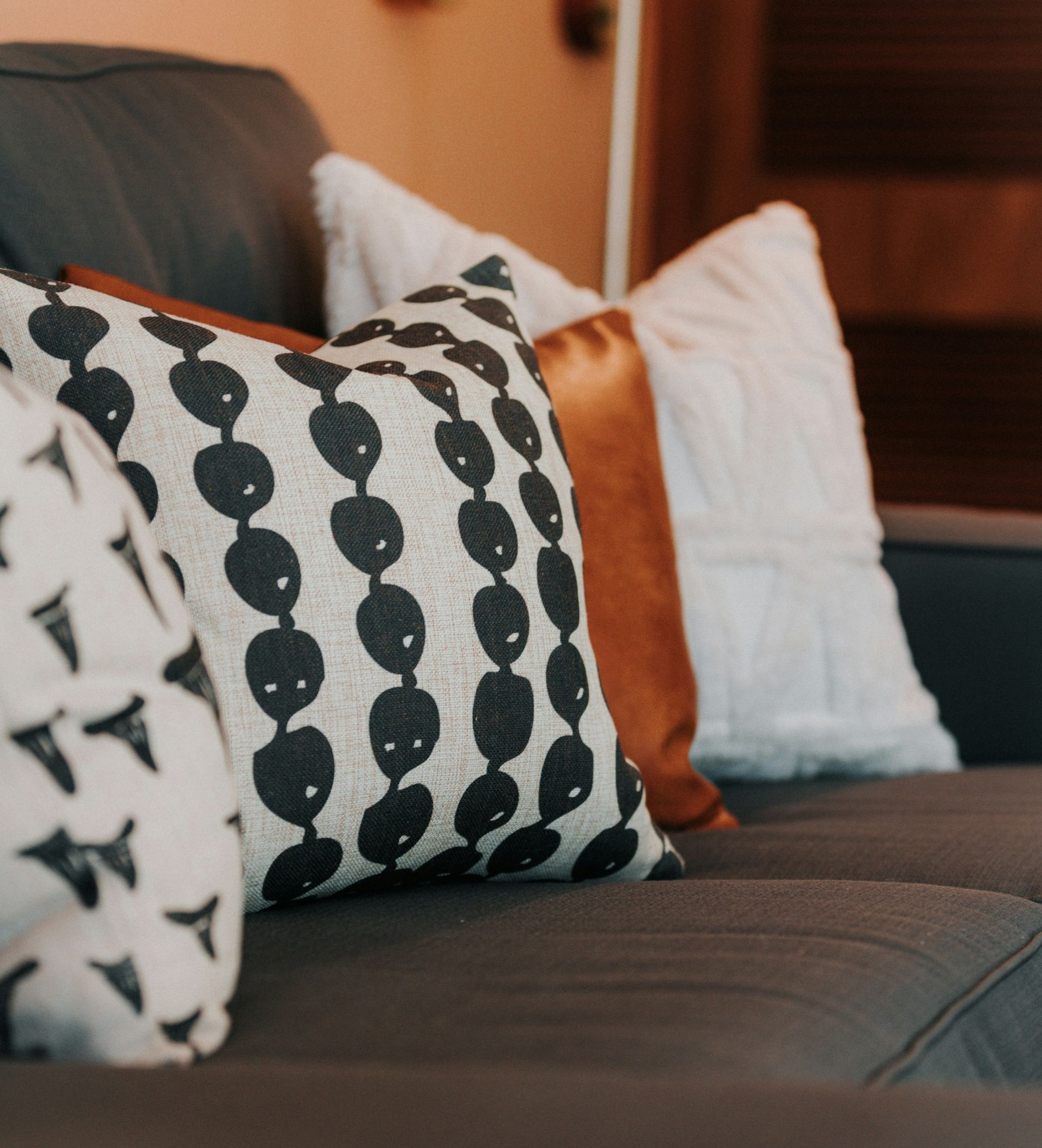 Decorative throw pillows with geometric and solid patterns arranged on a dark sofa.