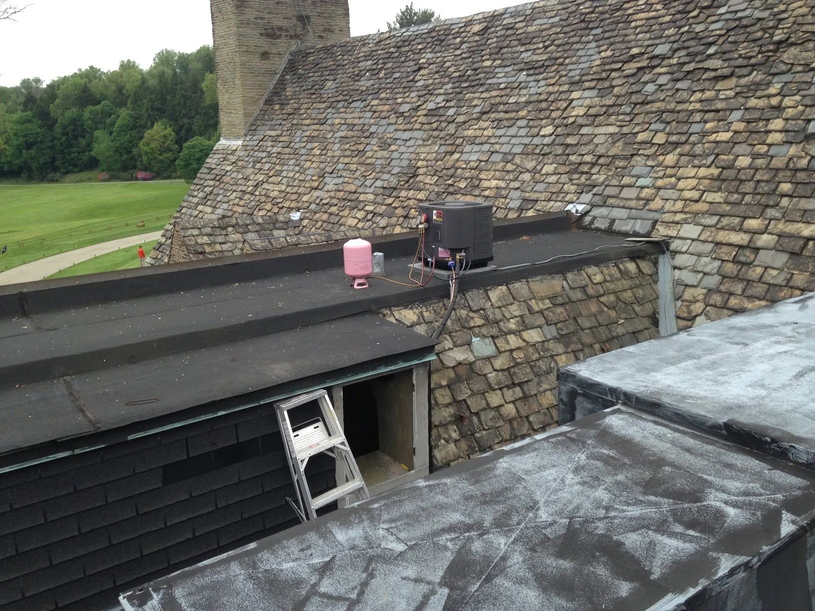 Rooftop with stone chimney, black roof, ladder opening, and pink bucket beside rooftop equipment.