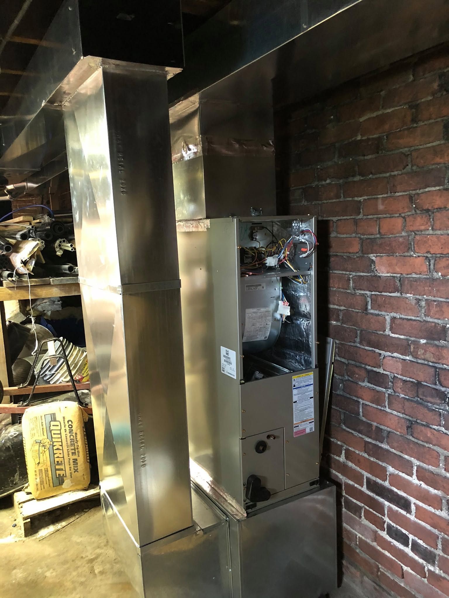 Damaged HVAC furnace in a partially exposed wall cavity with ductwork and brick wall nearby