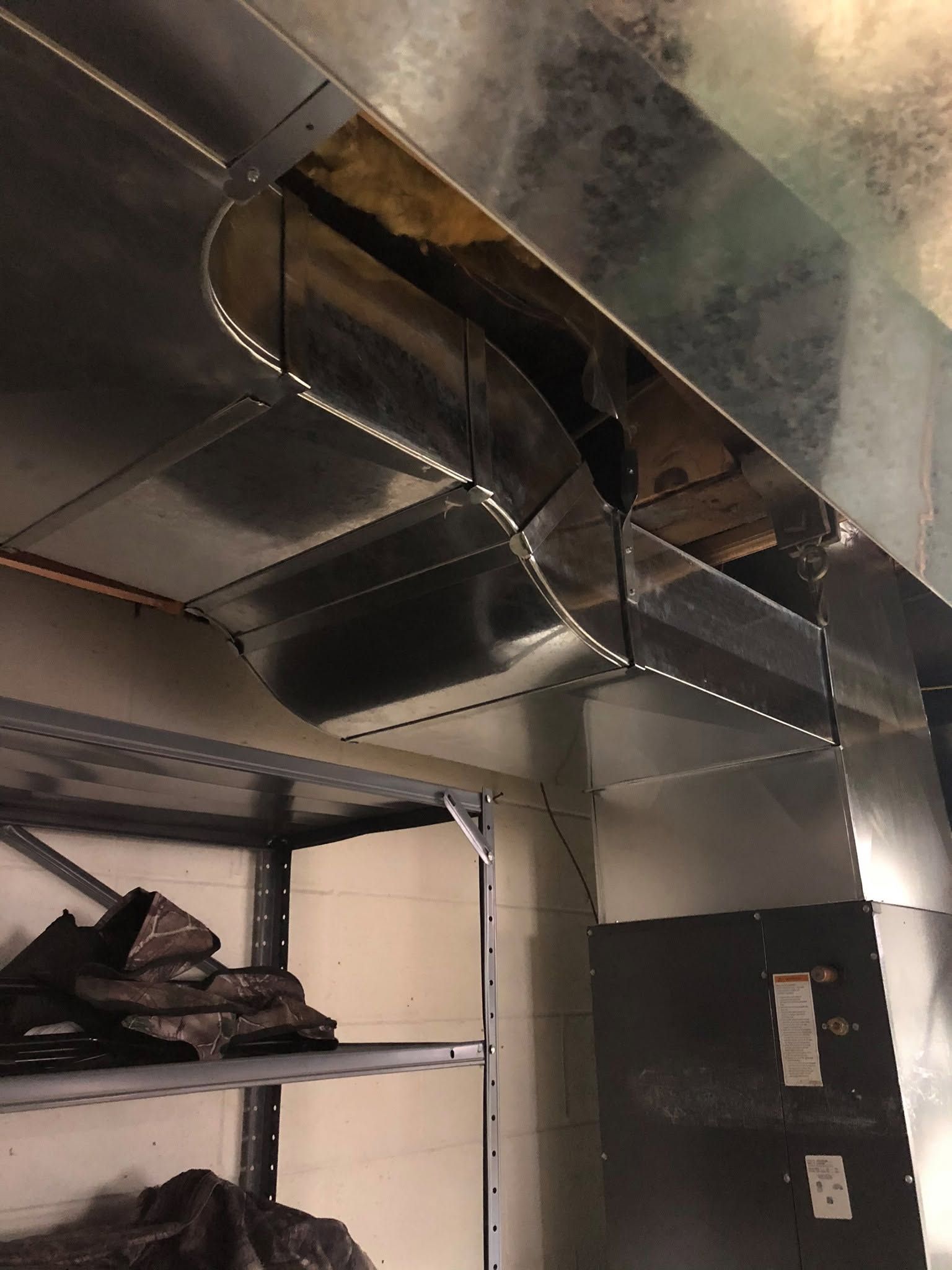 Ceiling HVAC ductwork in a utility room above shelves and stacked bags.