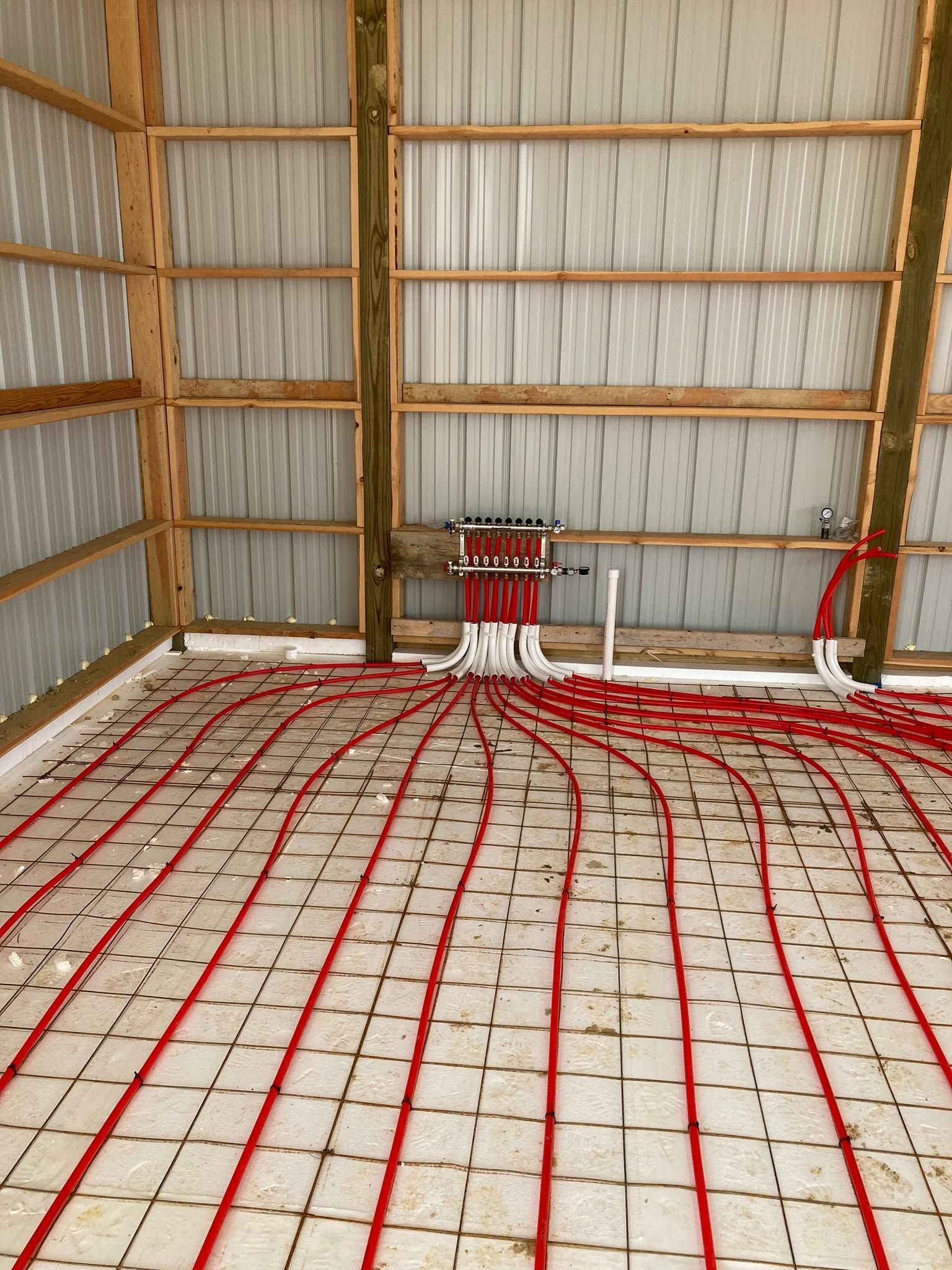 Interior of a barn under construction with red radiant floor tubing laid across the concrete floor