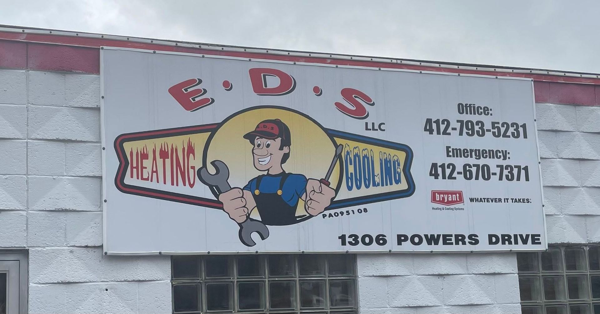 E.D.’s Heating & Cooling sign on a building, with cartoon technician and phone numbers.