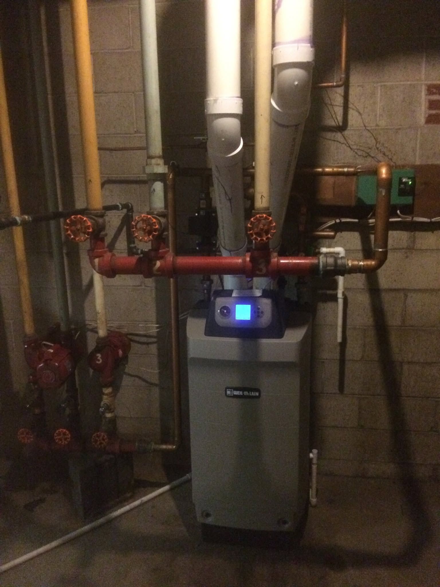 Heating boiler with red pipes and a blue-lit control panel in a basement utility room