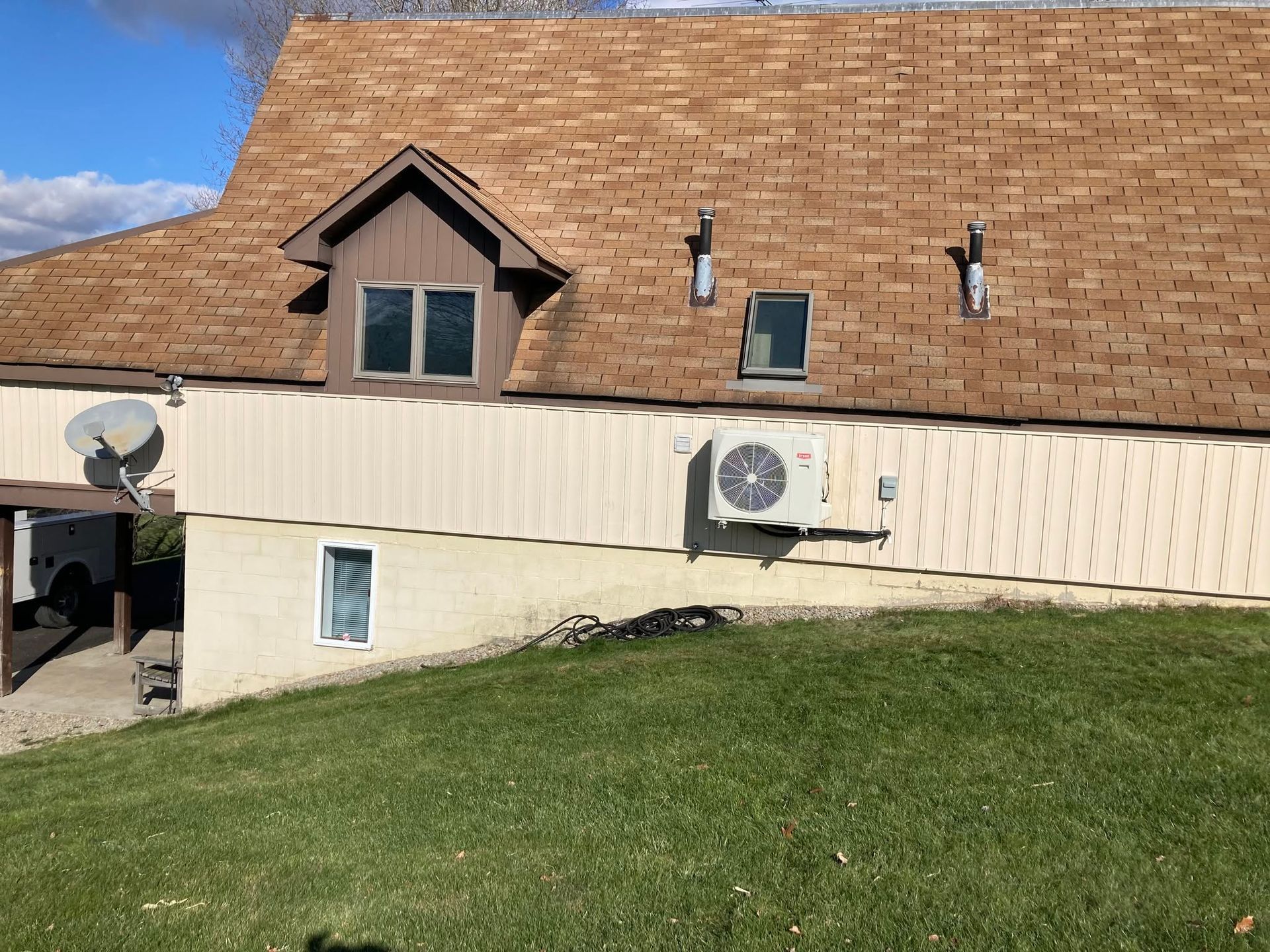 House exterior with brown shingle roof, dormer window, wall-mounted AC units, and a grassy lawn.