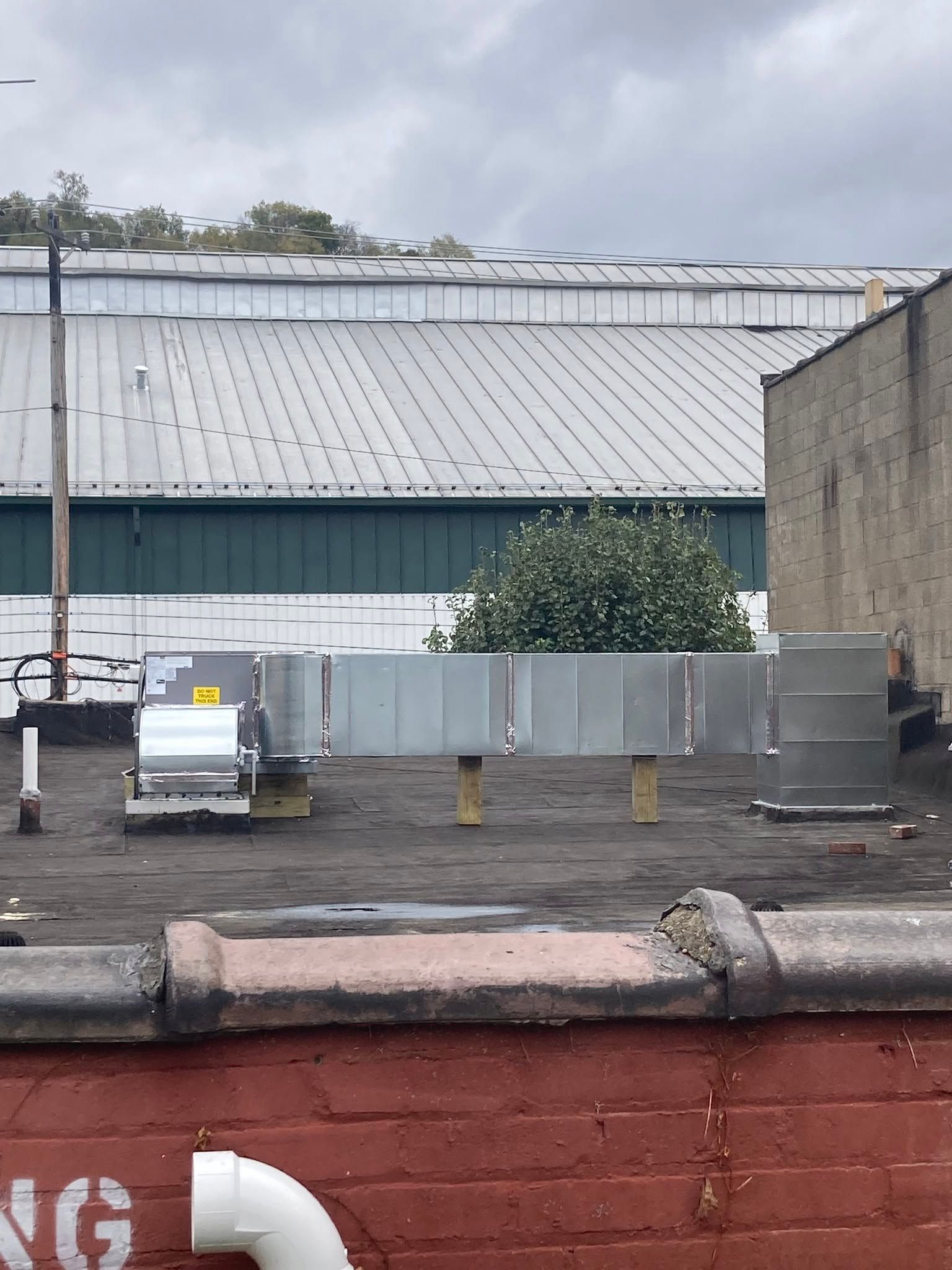 Industrial yard with a large metal-roofed warehouse, gray containers, and a white utility vehicle behind a red wall.