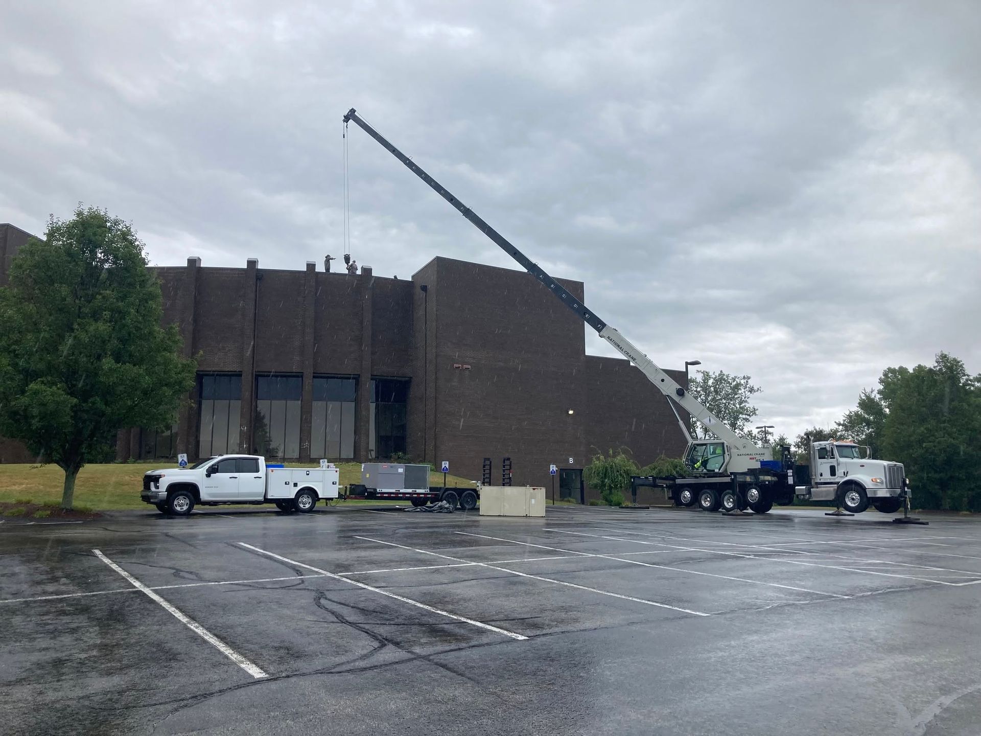 Workers and trucks outside a brick building with a crane lifting debris under cloudy skies