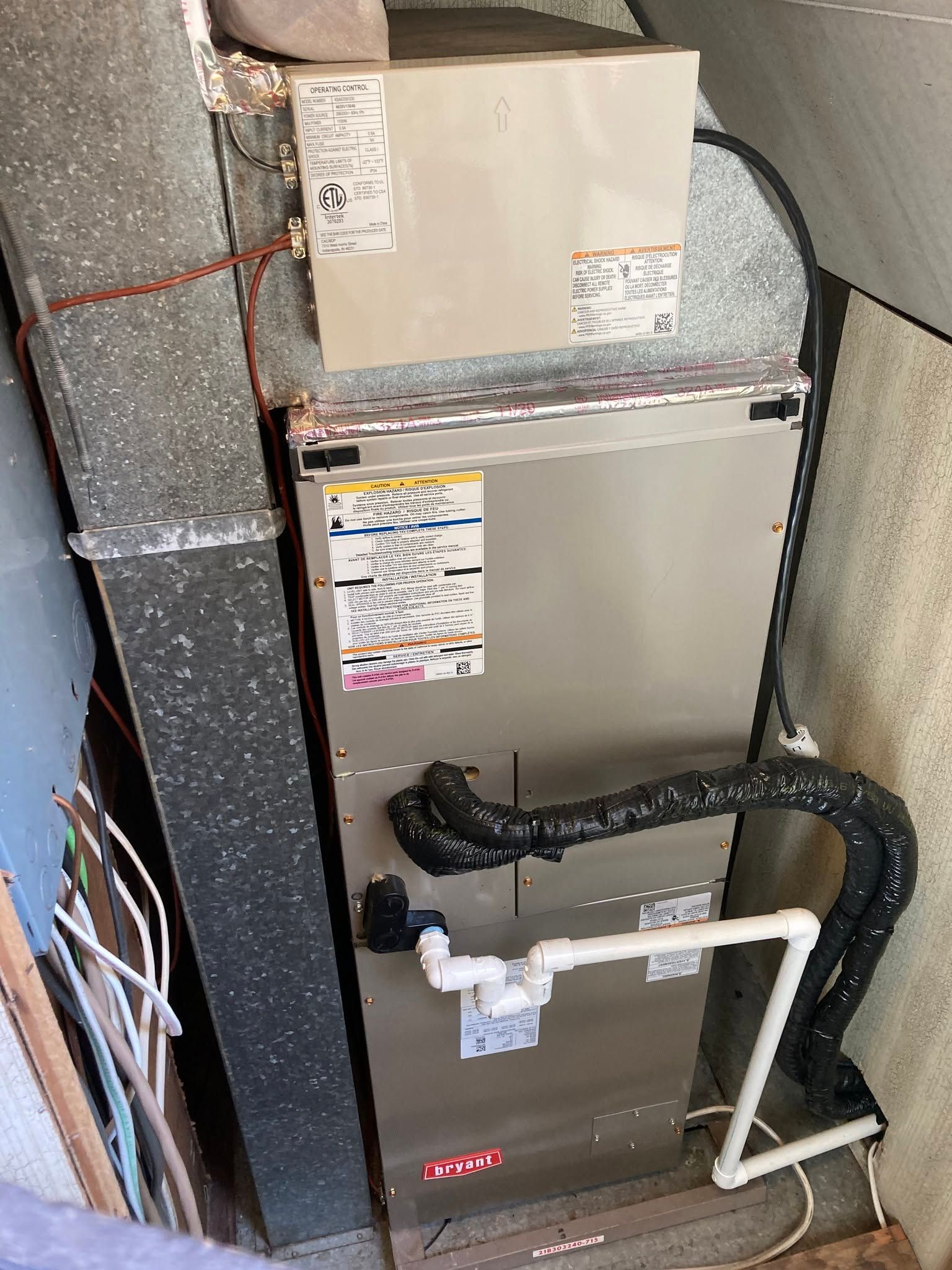HVAC furnace and ductwork in a utility closet with exposed pipes and wiring