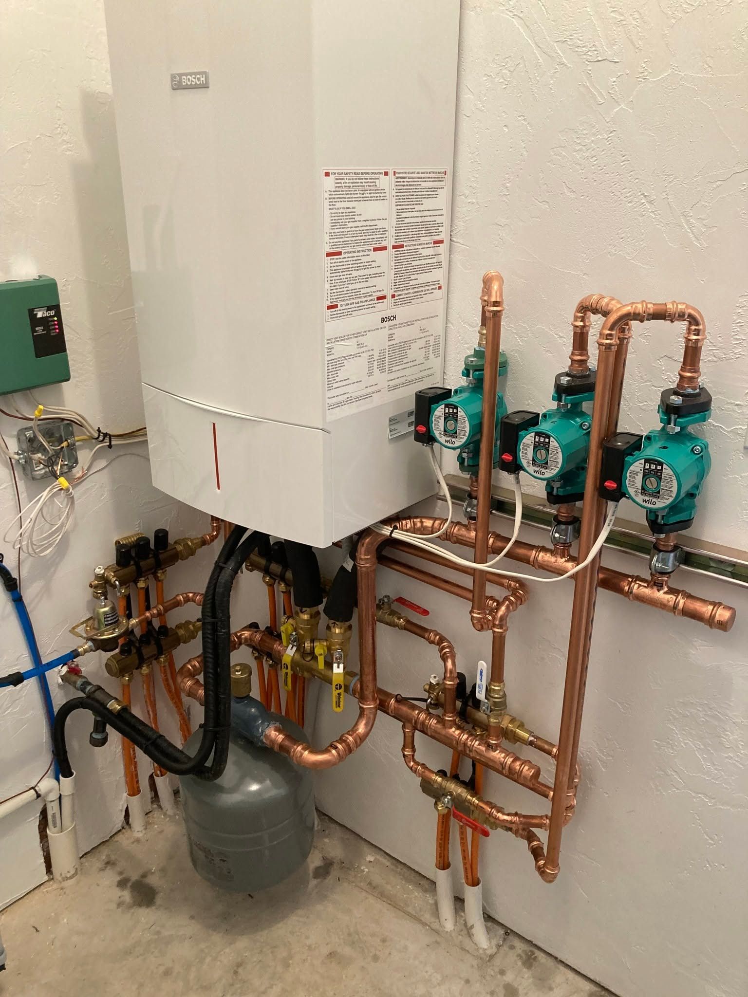 Wall-mounted boiler with copper plumbing, pumps, and valves in a utility room