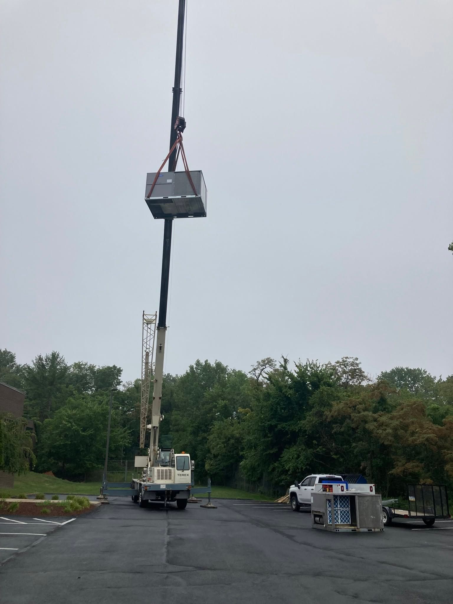 Crane lifting a small platform above a paved lot with workers and vehicles below.