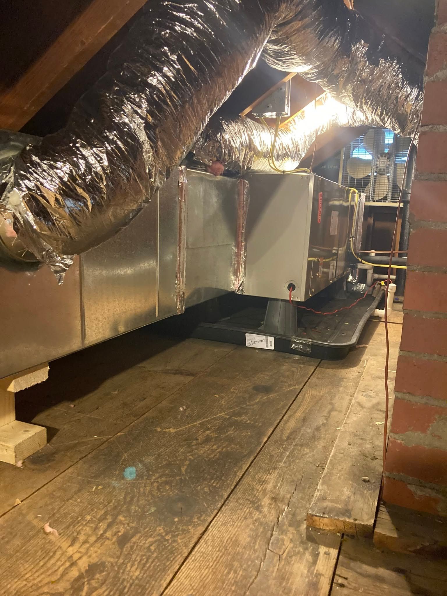 Attic crawlspace with insulated HVAC ducts, exposed floor joists, and a furnace unit near a brick wall