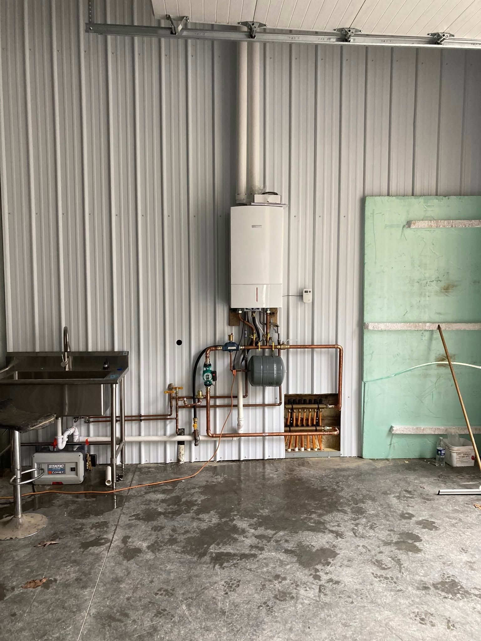 Industrial room with wall-mounted boiler, exposed pipes, and a green door on a concrete floor
