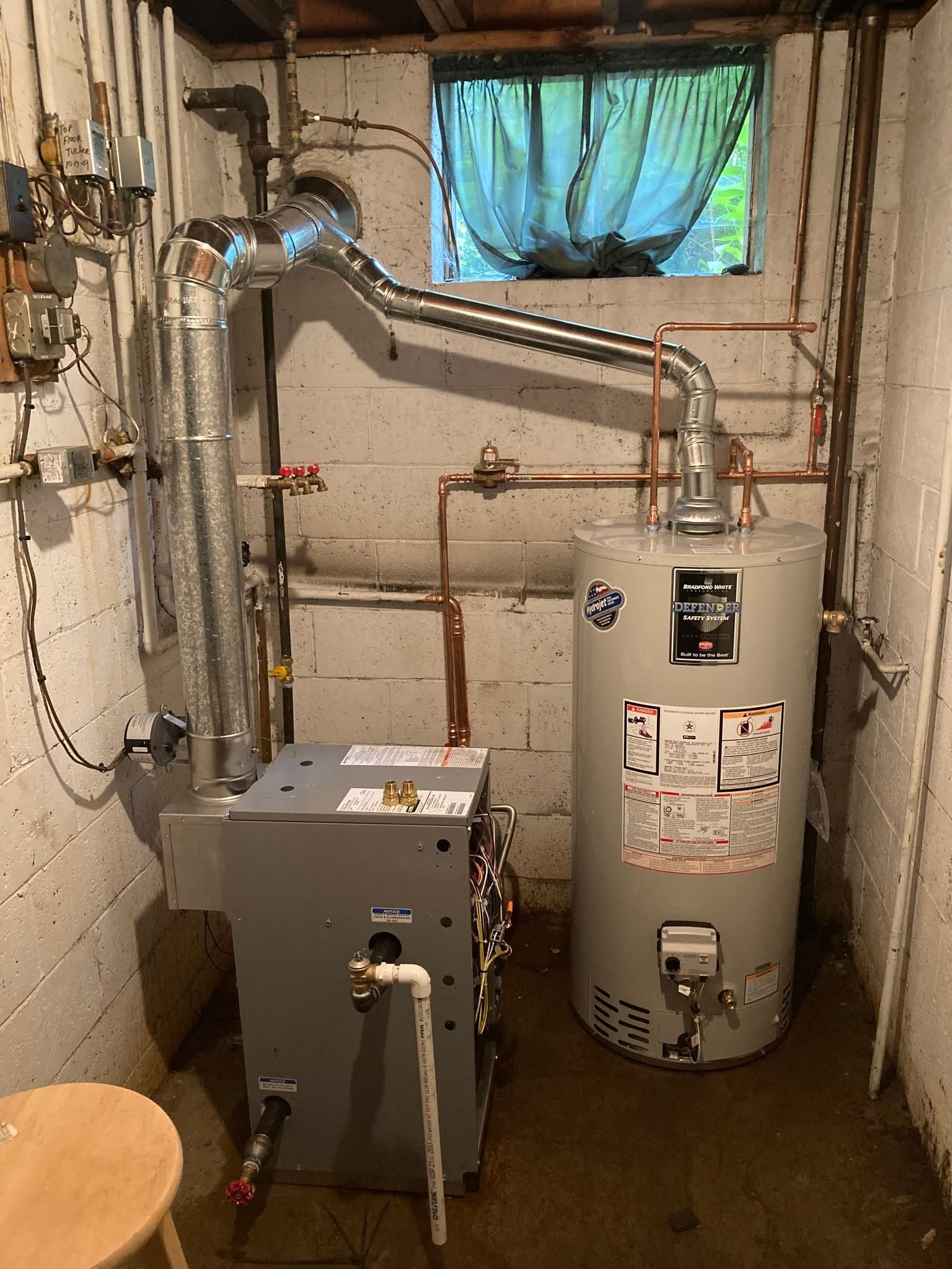 Basement utility room with a water heater, boiler, pipes, and a small window.