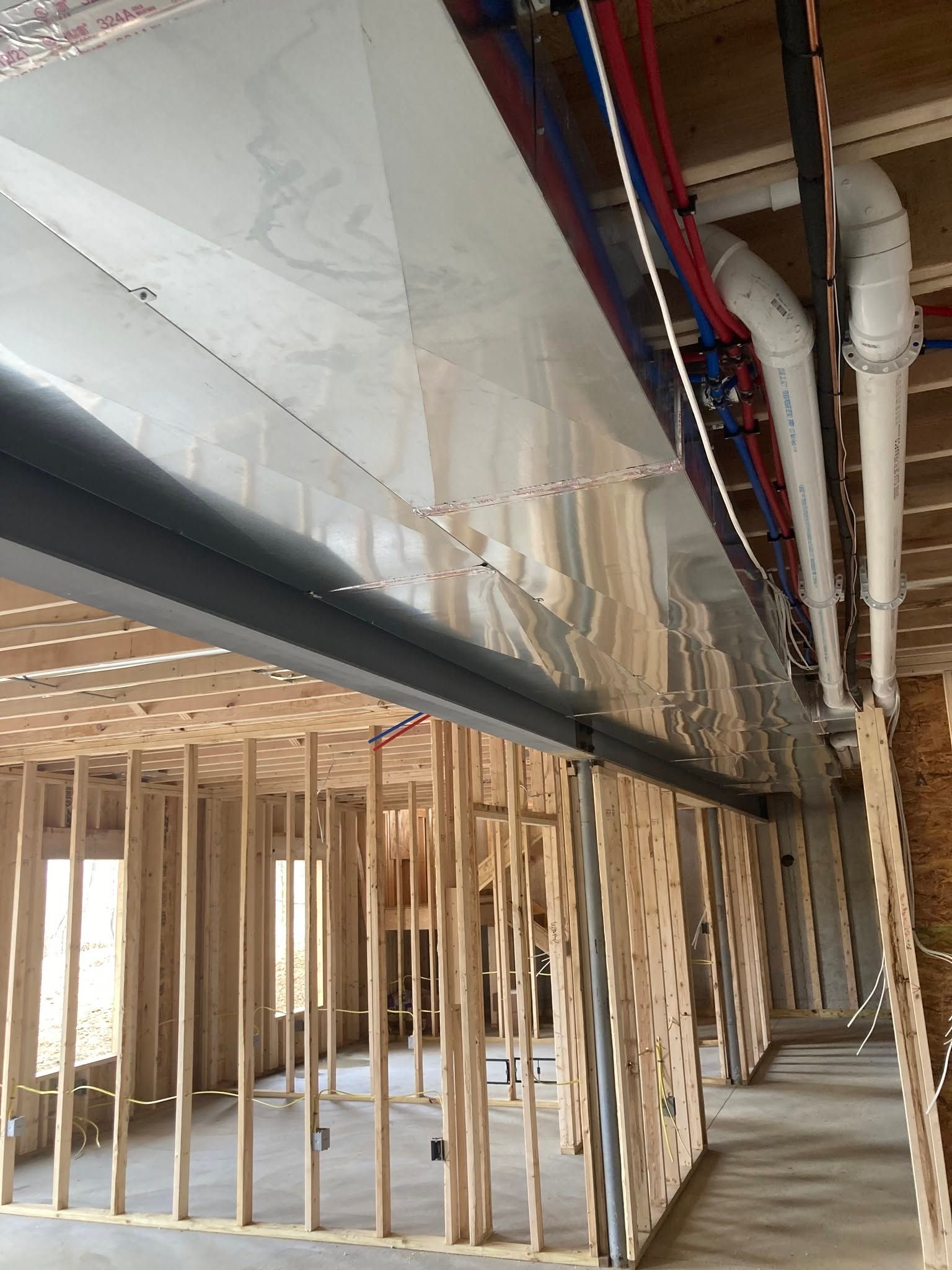Interior construction site with exposed wooden framing, ductwork, and pipes under a partially finished ceiling
