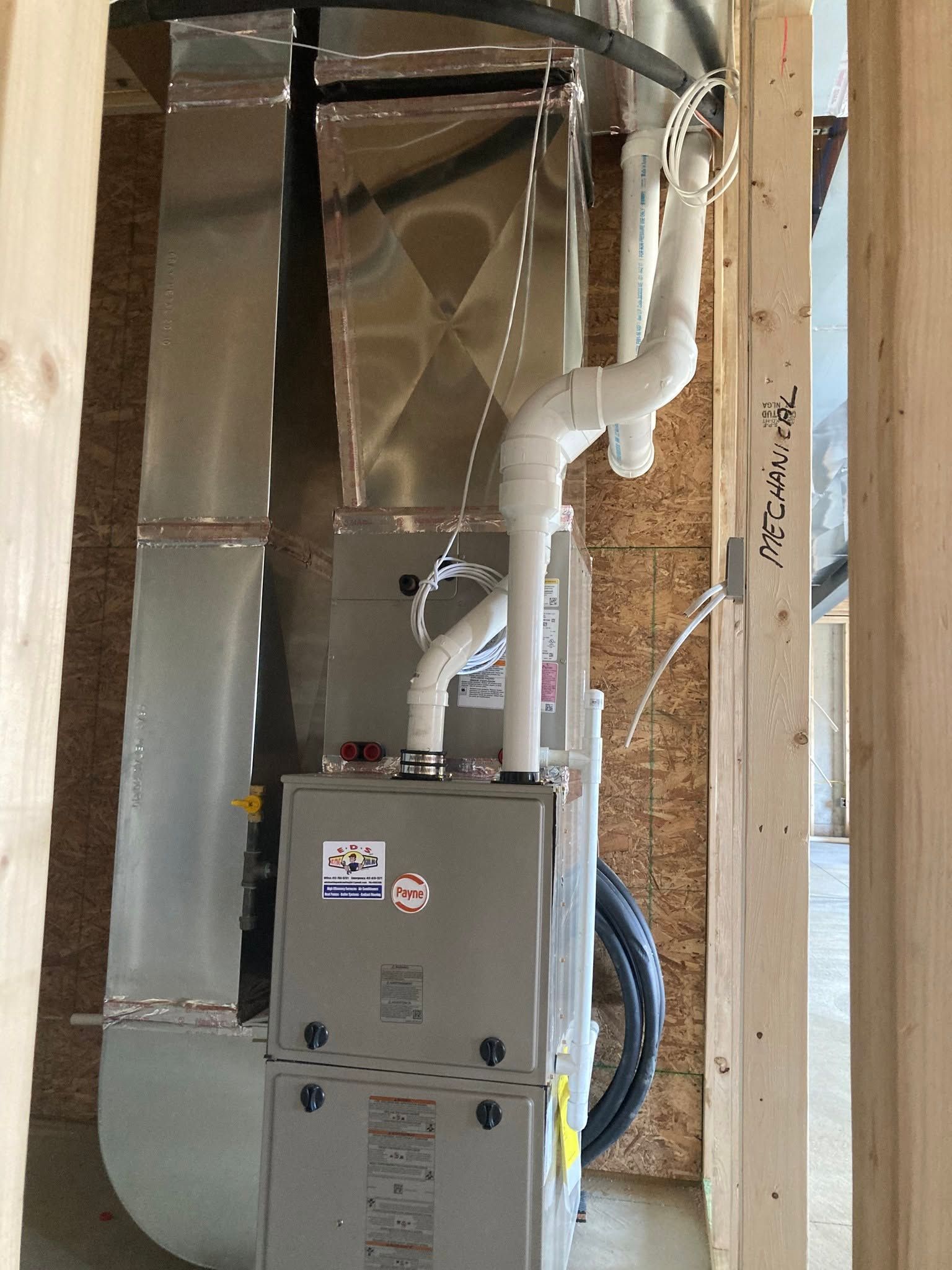 Gray HVAC unit with white insulated ducting in an unfinished indoor utility space.