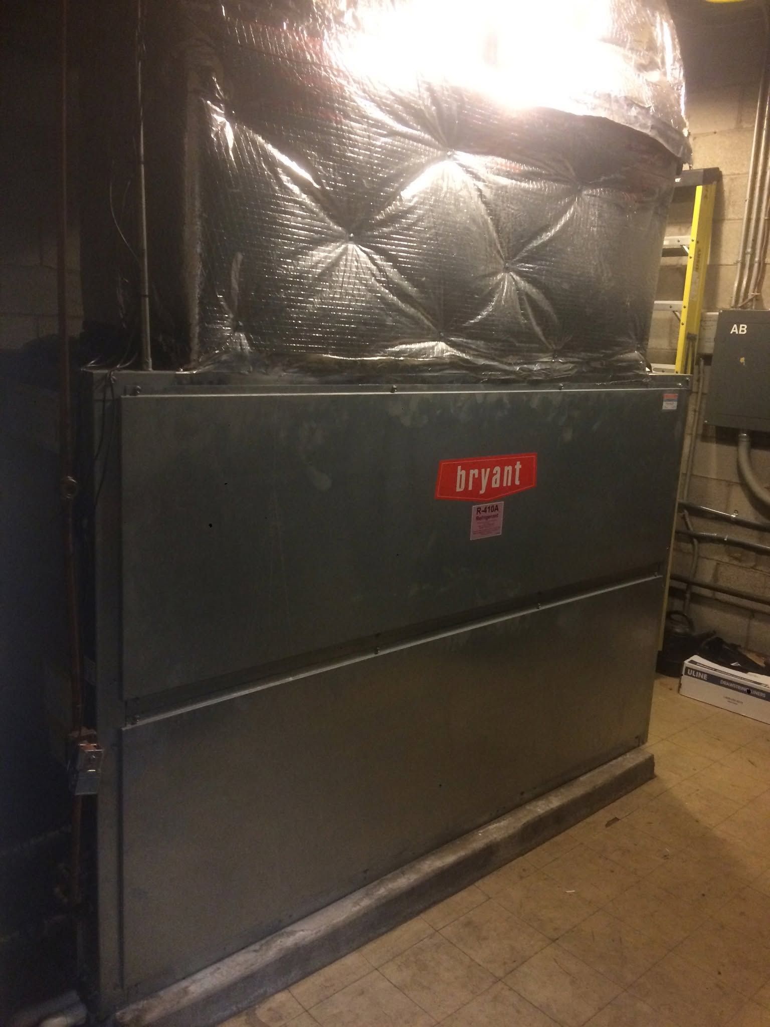 Large gray HVAC unit with wrapped ductwork in an industrial room.