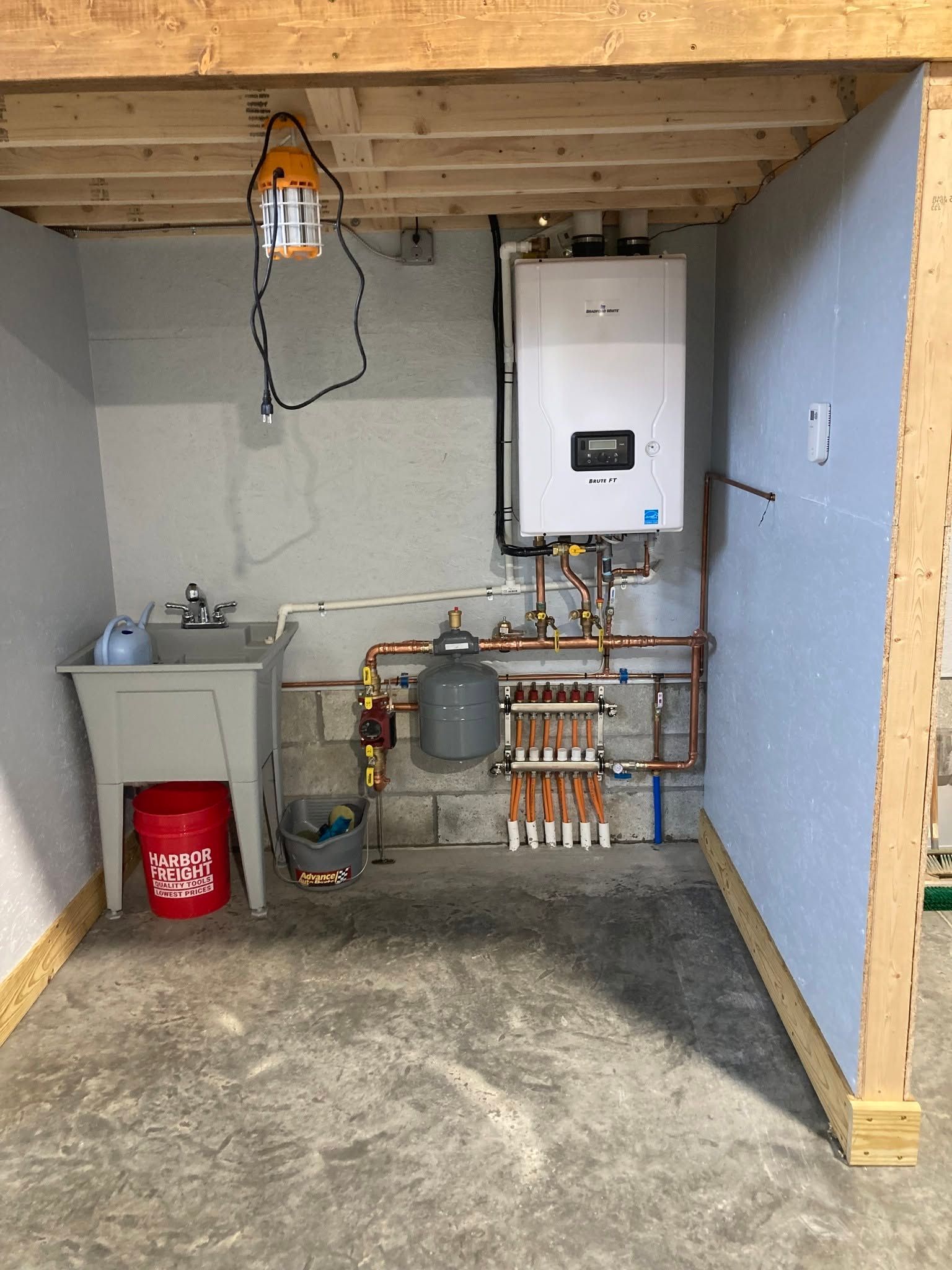 Basement utility room with water heater, plumbing manifold, sink, and exposed ceiling beams