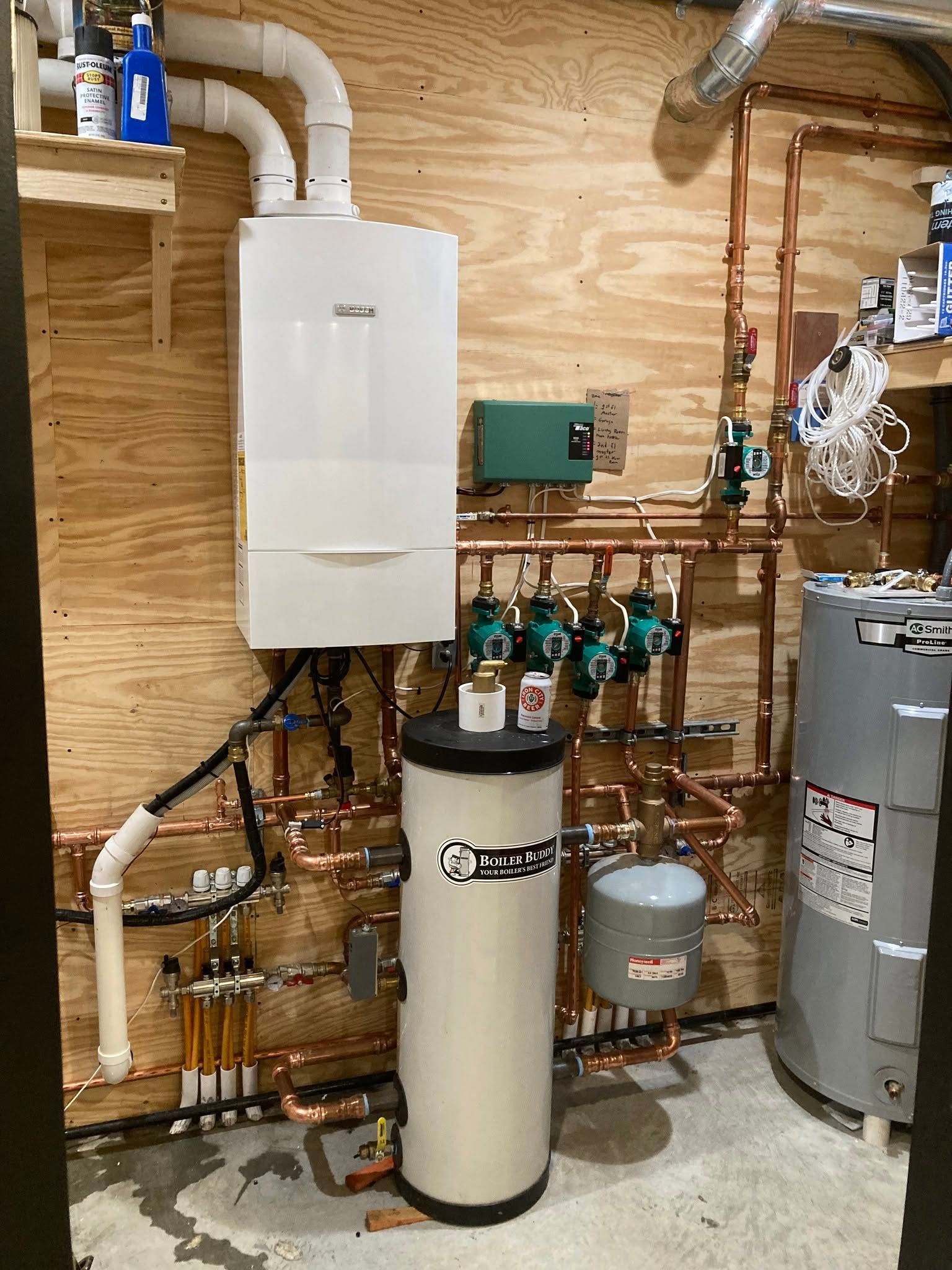 Boiler room with wall-mounted white unit, tanks, pipes, and plumbing equipment on wood-paneled wall
