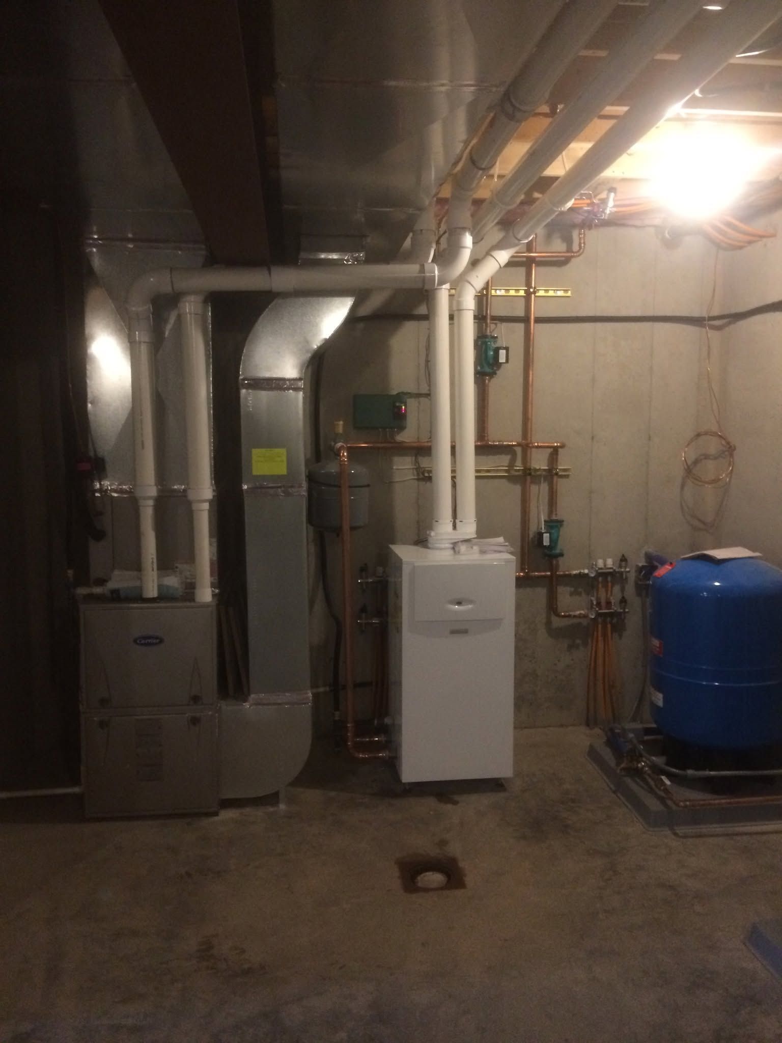 Basement utility room with furnace, pipes, water heater, blue tank, and overhead lighting.