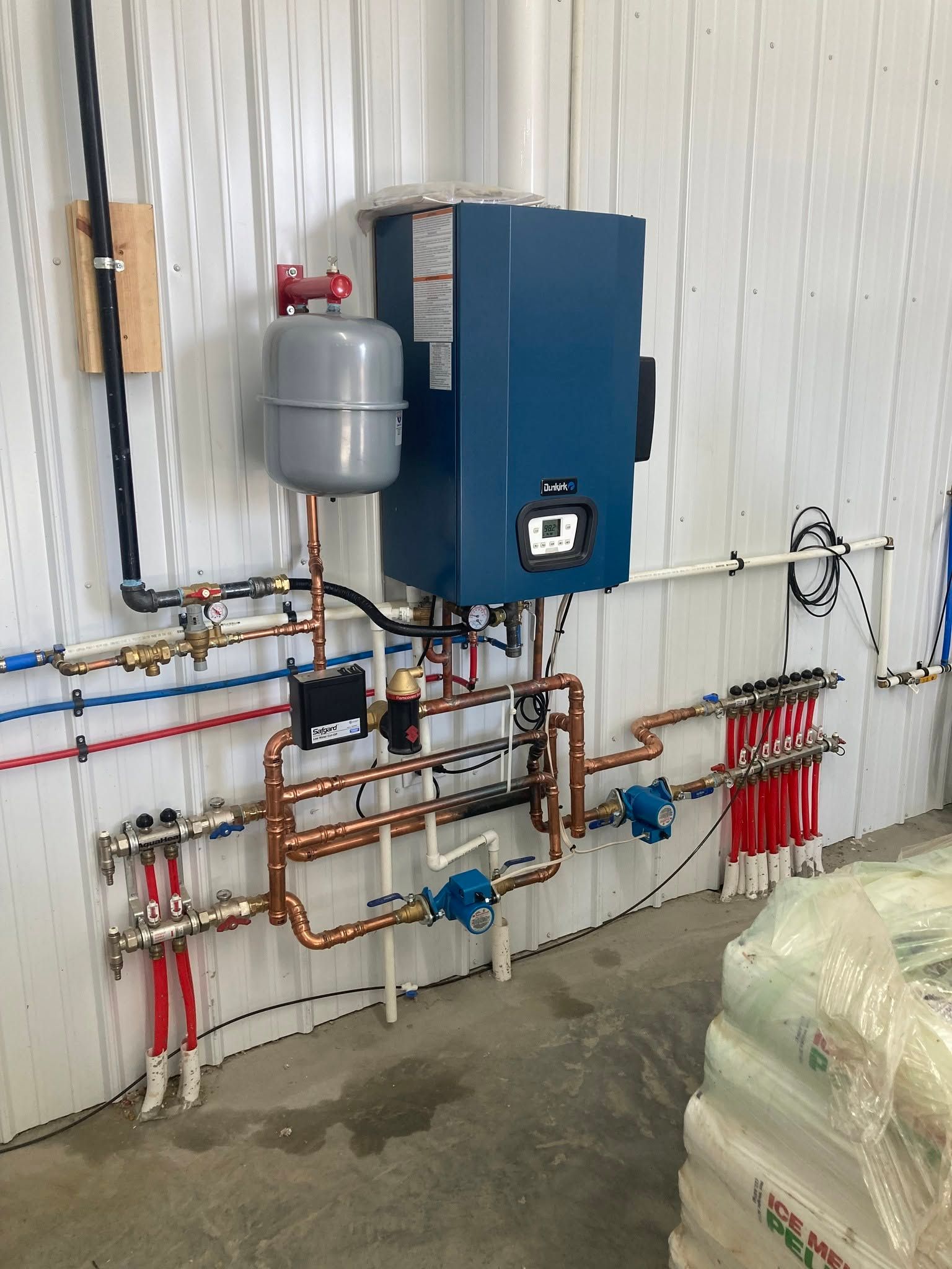 Wall-mounted boiler and plumbing manifold with copper pipes and red valve handles in a utility room