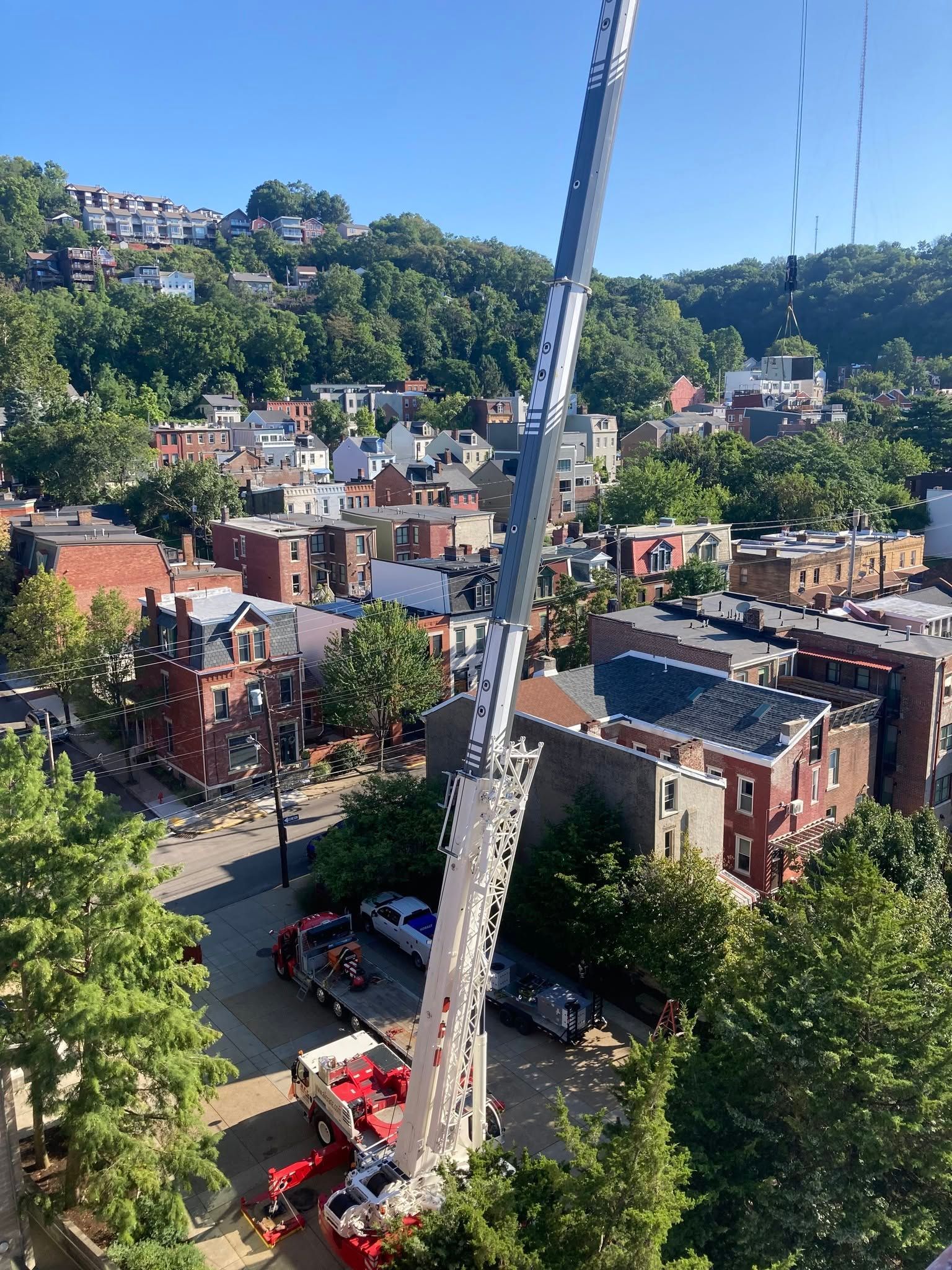 Tall white crane over a brick neighborhood with trees and hills in the background