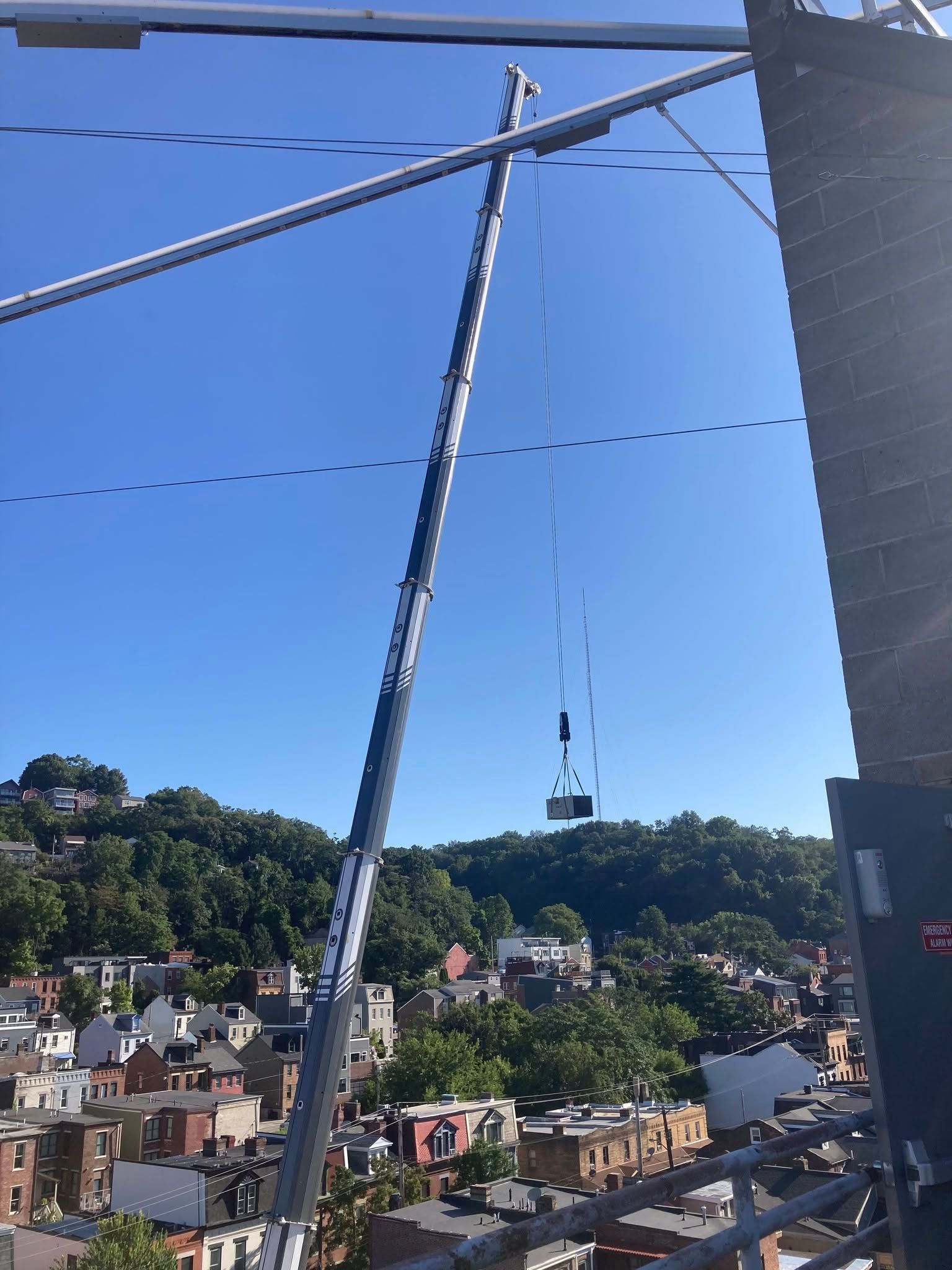 Crane lifting a person or platform over a hillside town under a clear blue sky