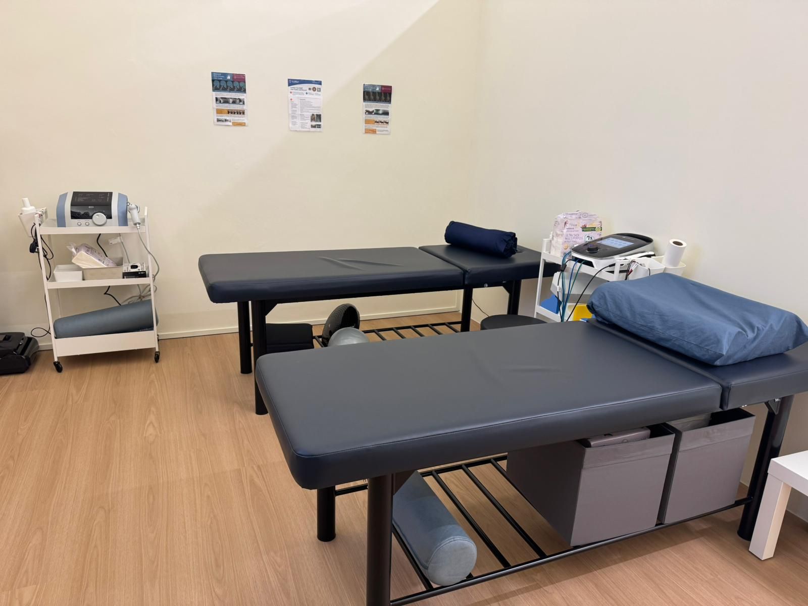 Clinic treatment room with two exam tables, a rolling cart, and medical supplies