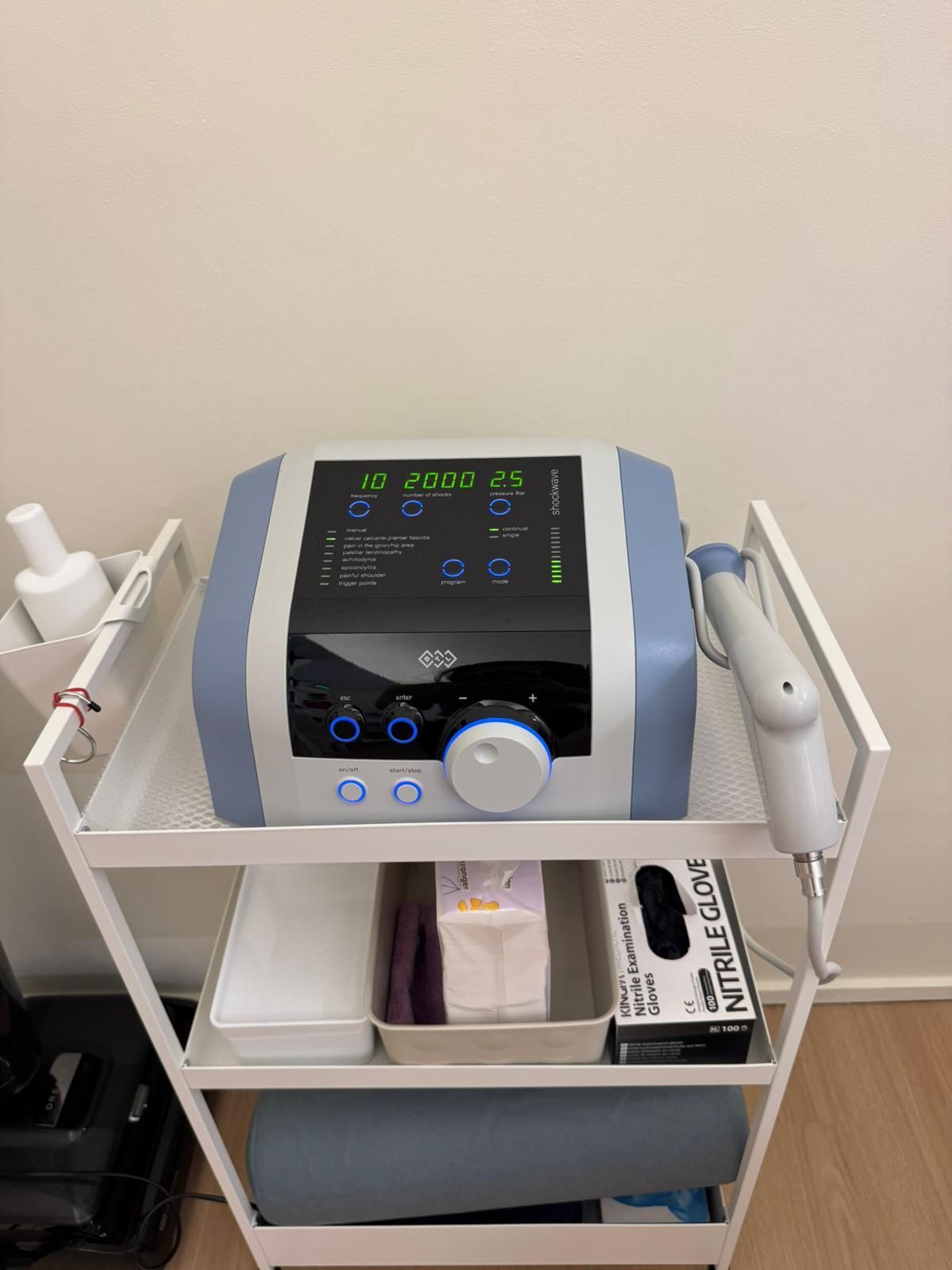 Medical device with digital display and control knob on a tray cart, with supplies stored below.