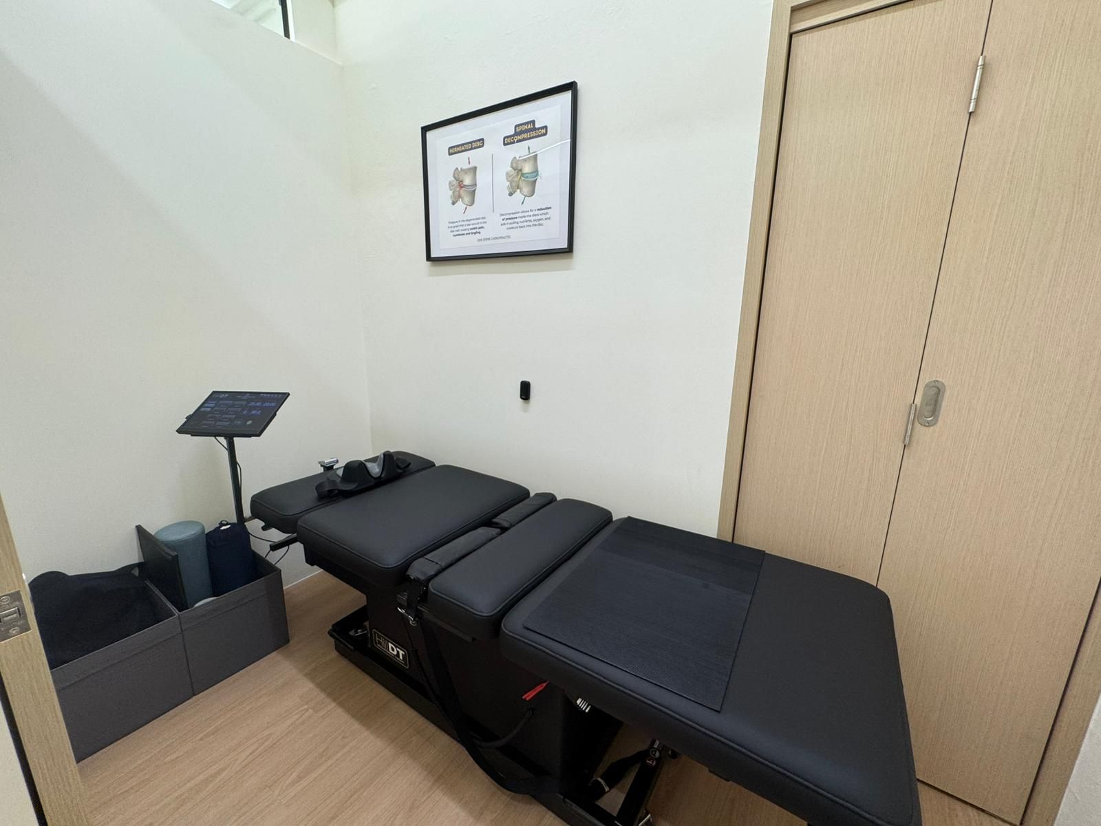 Empty chiropractic exam room with black treatment table, poster, and blinds.