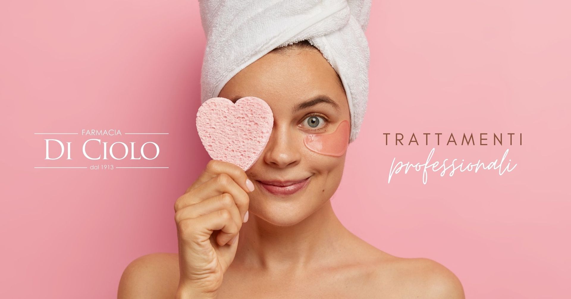 Una donna con un asciugamano sulla testa tiene una spugna a forma di cuore su un occhio, su uno sfondo rosa. La scritta recita 
