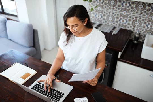 Woman smiling while talking on phone, taking notes at desk in office setting.