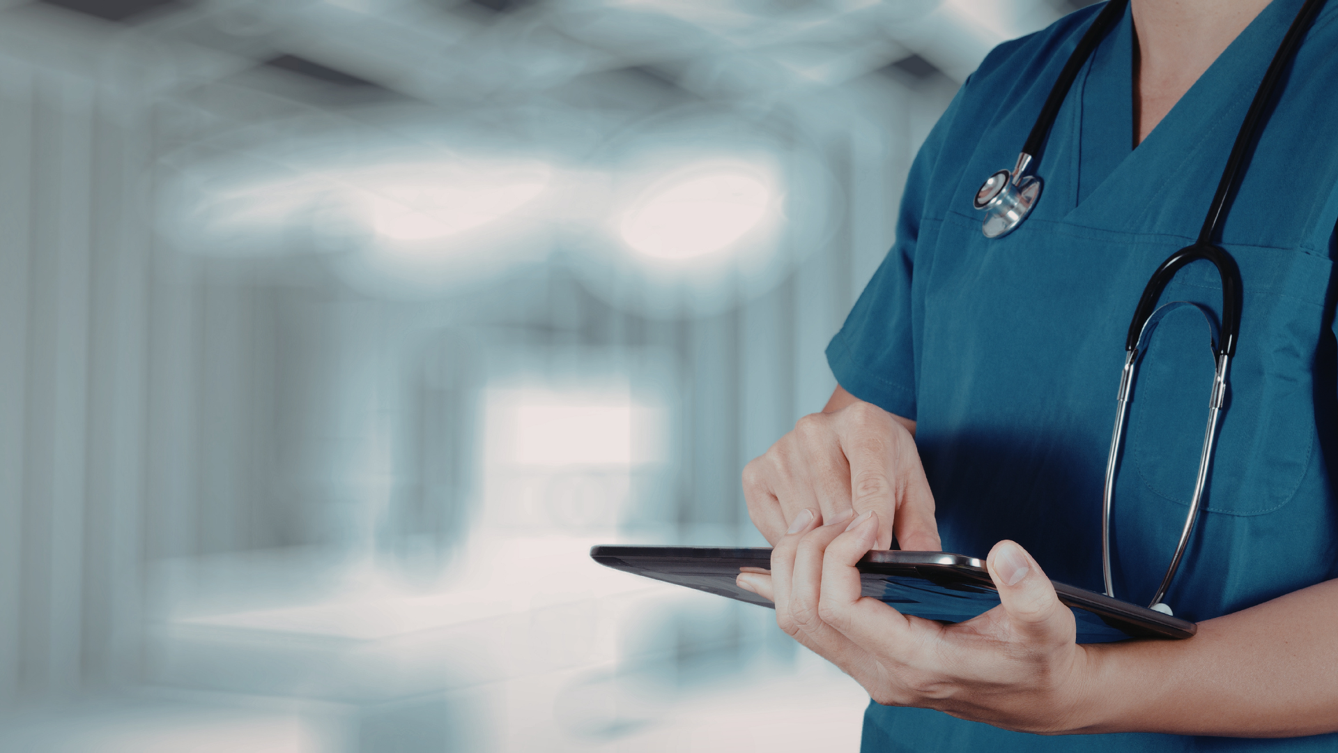 Doctor in blue scrubs using a tablet in a hospital hallway
