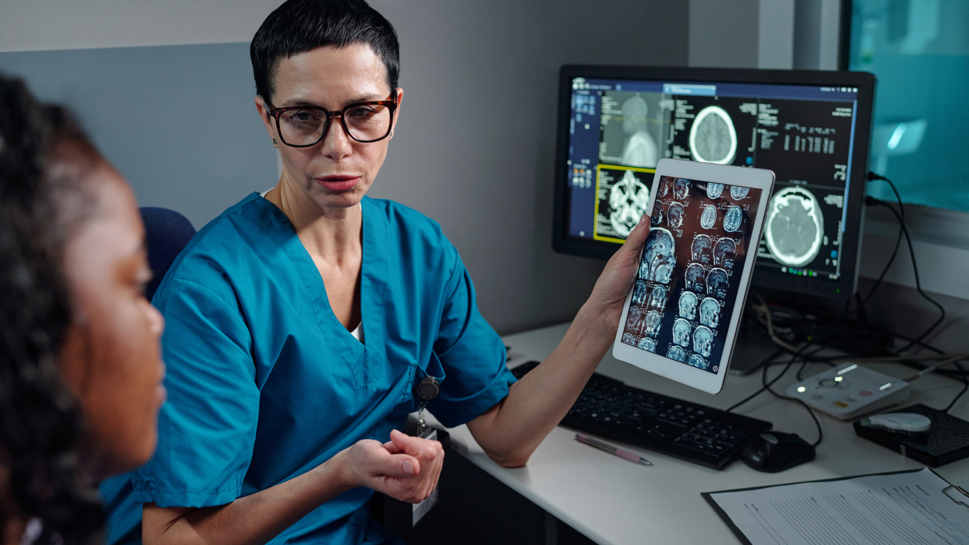 Doctor discussing brain scan images on a desktop monitor with a patient in a clinic office