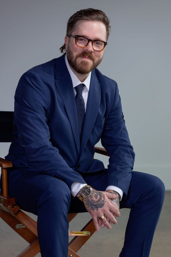A man sitting in a chair with a dark blue suit and stylish glasses