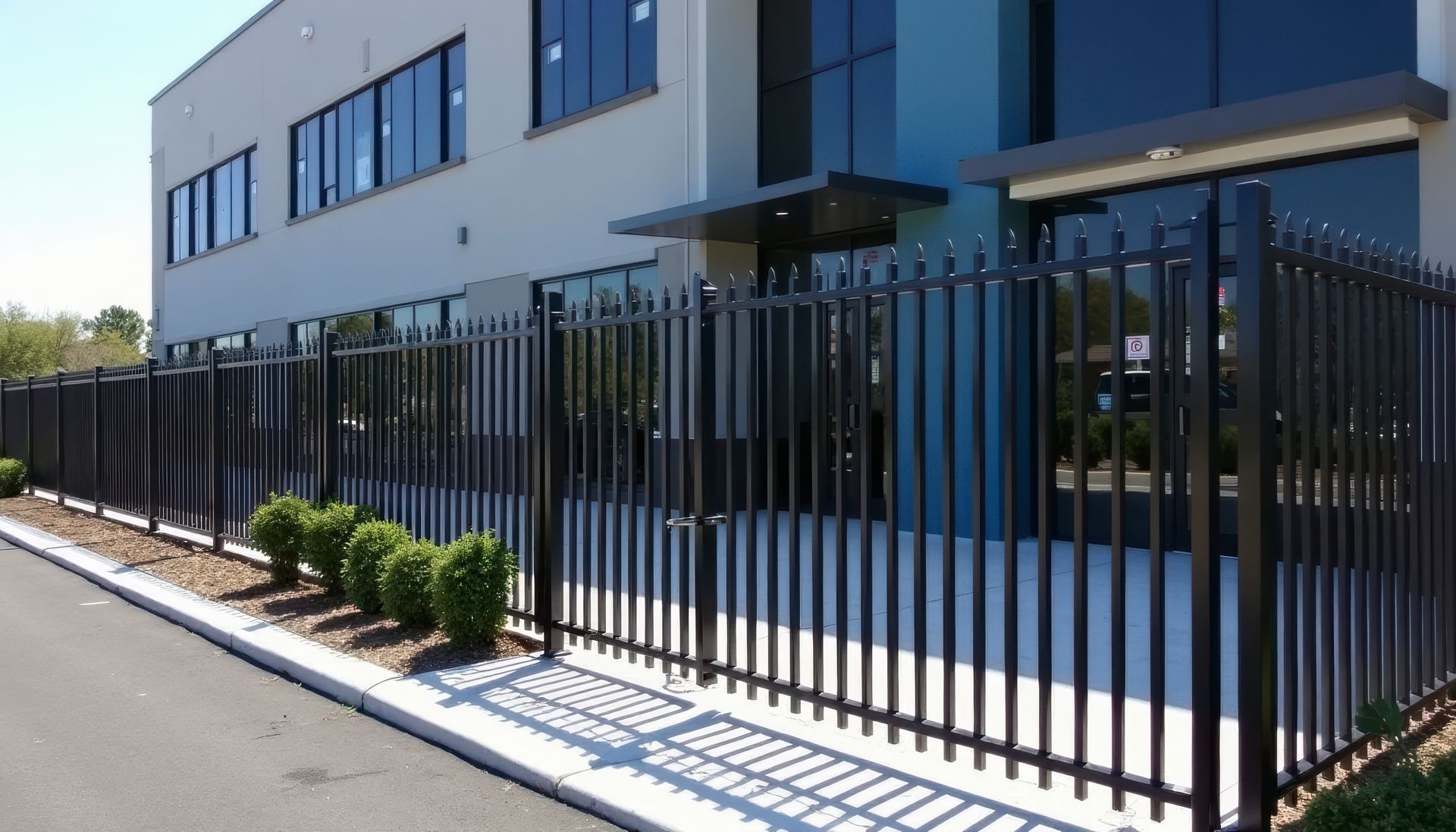 Black metal fence along a sidewalk beside a modern blue-and-white office building.
