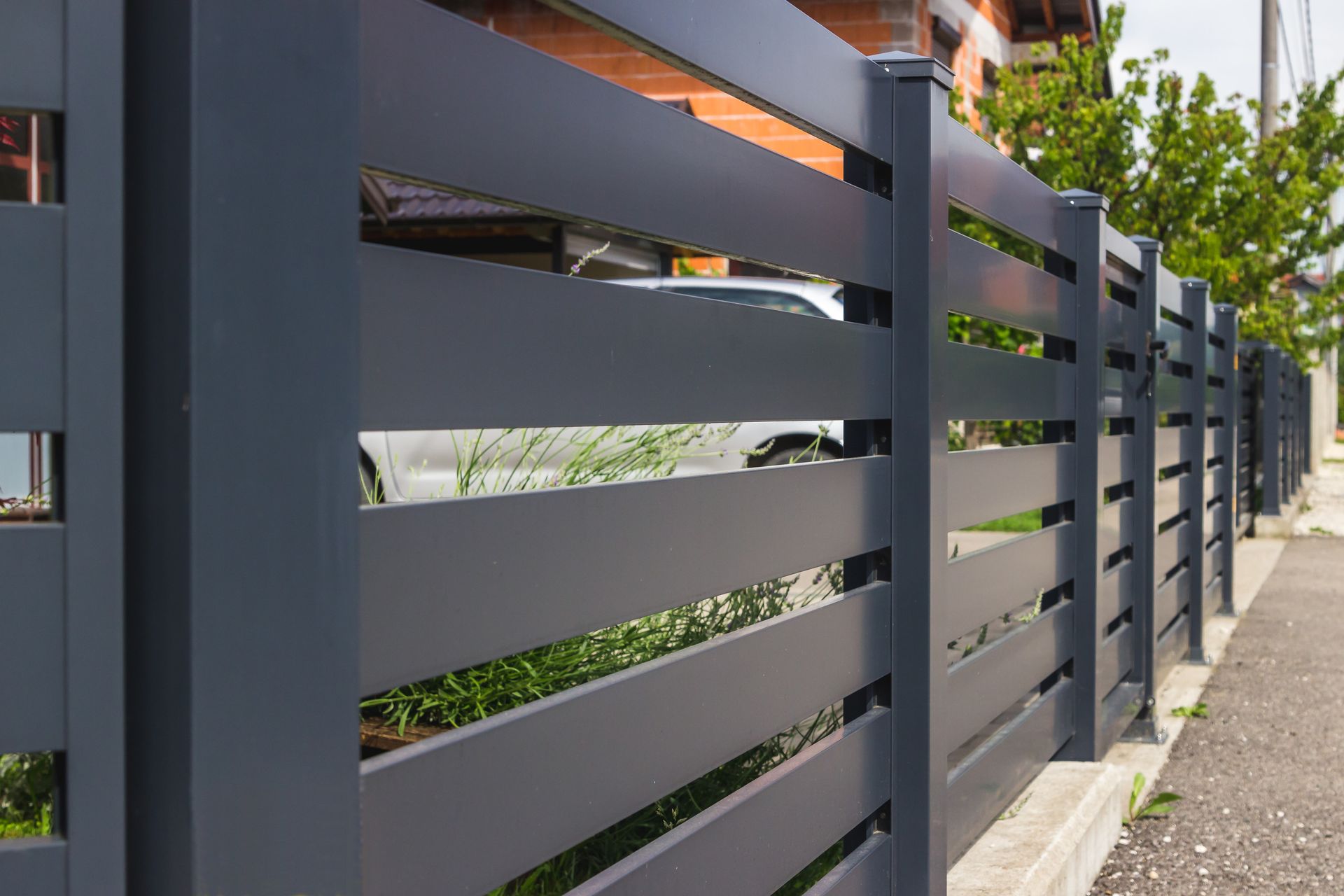 Modern gray horizontal slat fence beside a sidewalk with greenery and building balconies behind it